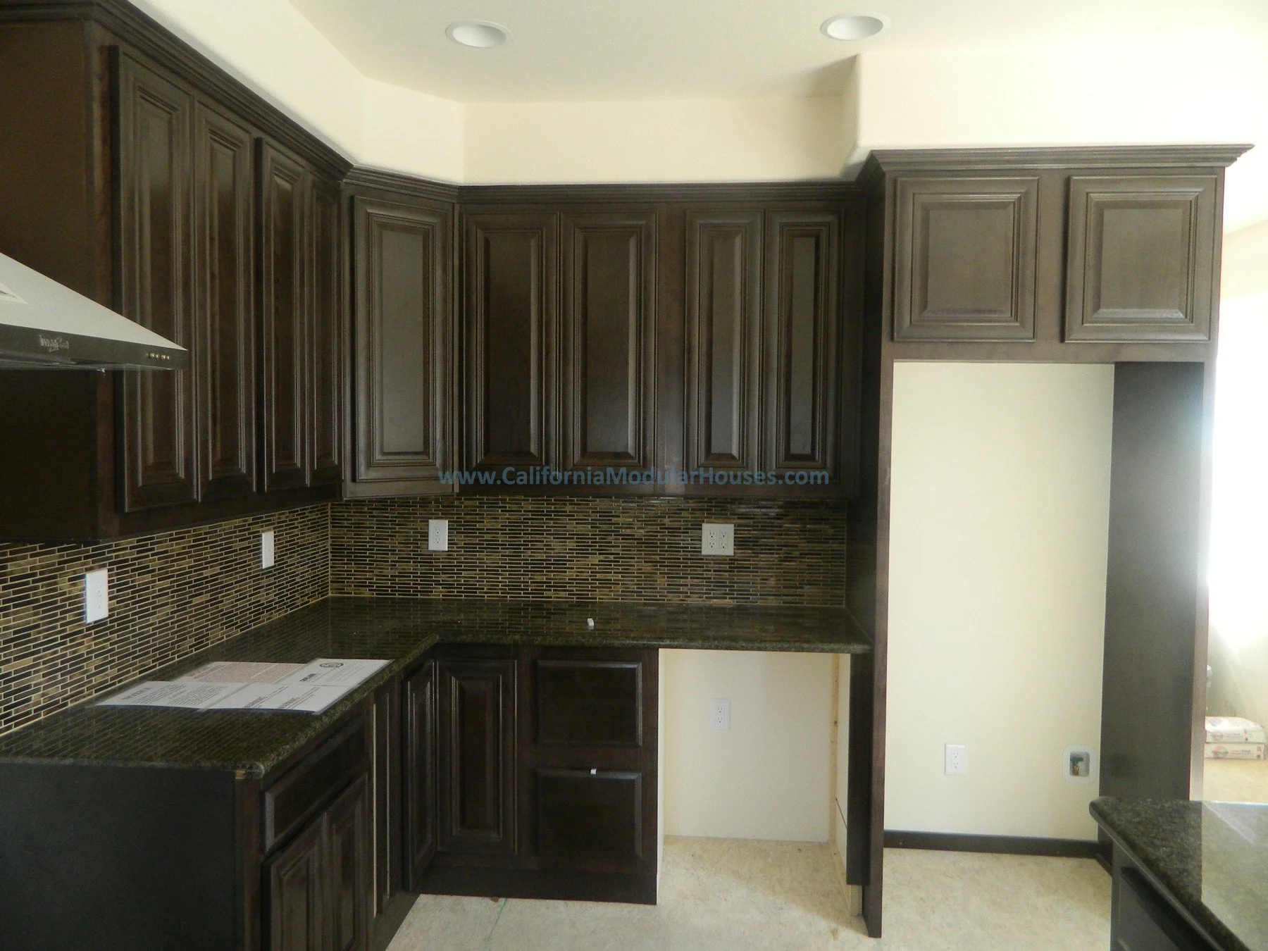 New kitchen with dark wood cabinets, granite countertops, a mosaic tile backsplash, and multiple electrical outlets.  The room is well-lit with ceiling lights.  Prefab Homes, Modular Homes Northern California, Prefab Houses.