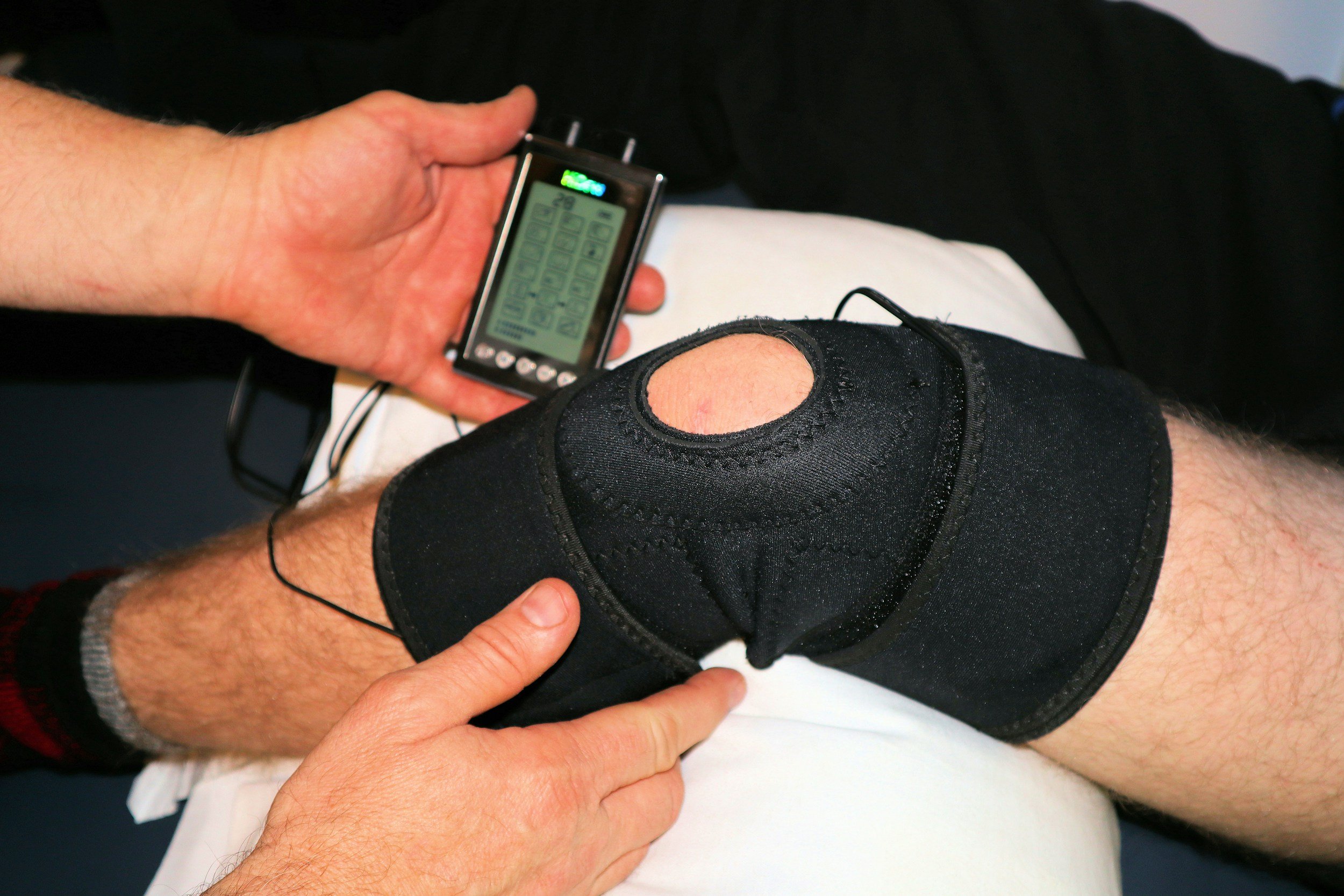 A person with a black knee brace and a digital pulse oximeter on their finger, showing oxygen levels, while resting.
