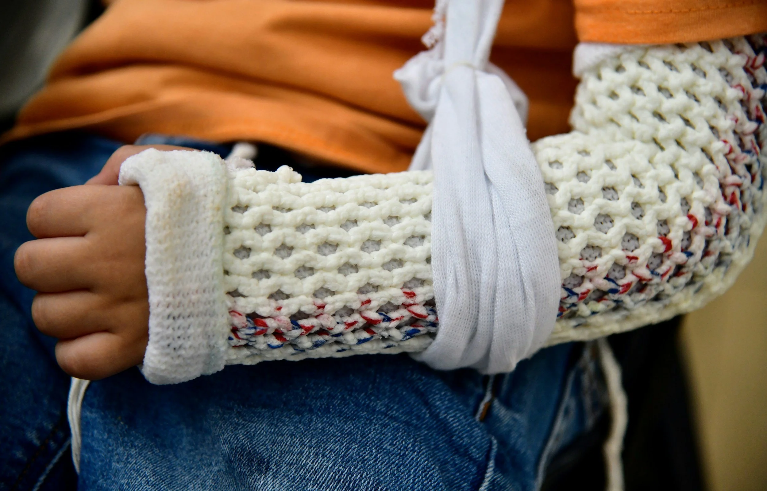 A person's arm in a white, knitted, textured sweater with a white medical bandage wrapped around the wrist.