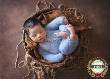 Newborn baby sleeping in a brown basket wrapped in a light blue knitted outfit with buttons.