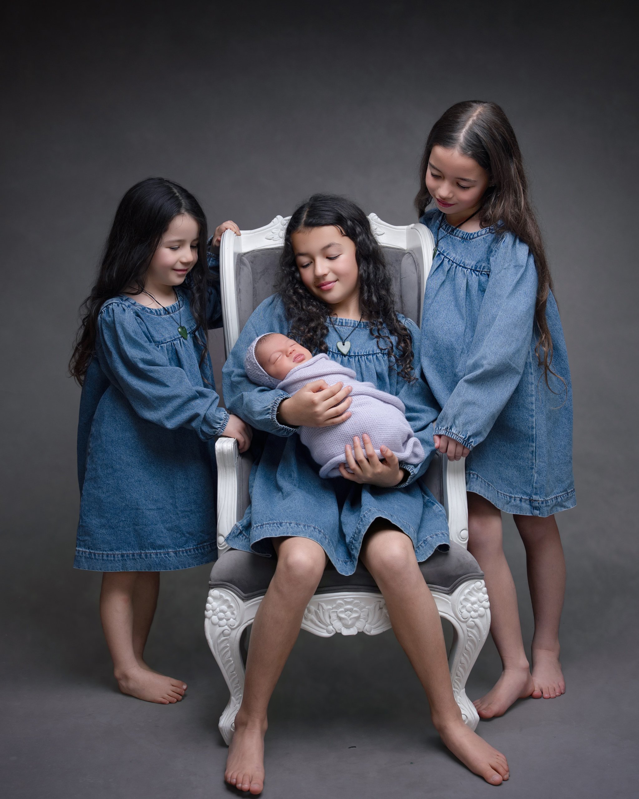 Three siblings cuddling their newborn baby during an Auckland newborn photography session.