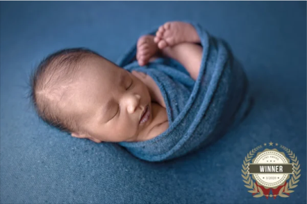 Close-up of a sleeping newborn wrapped in a blue blanket on a blue surface.