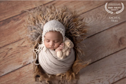 Adorable sleeping baby wrapped in a blanket with a fluffy headband, lying on a wooden floor with a textured rug around them.