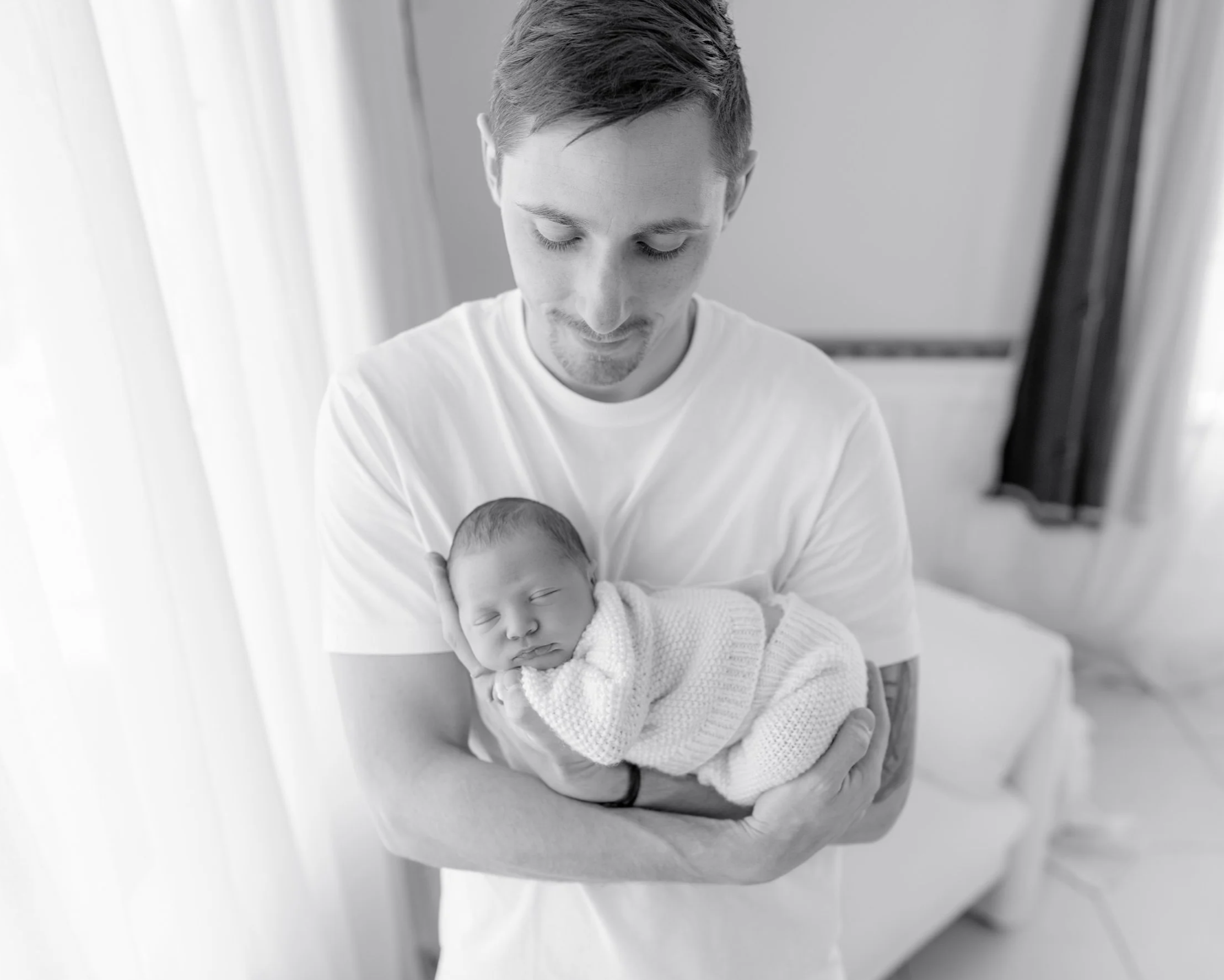 Father gently holding his sleeping newborn baby during a natural lifestyle newborn session