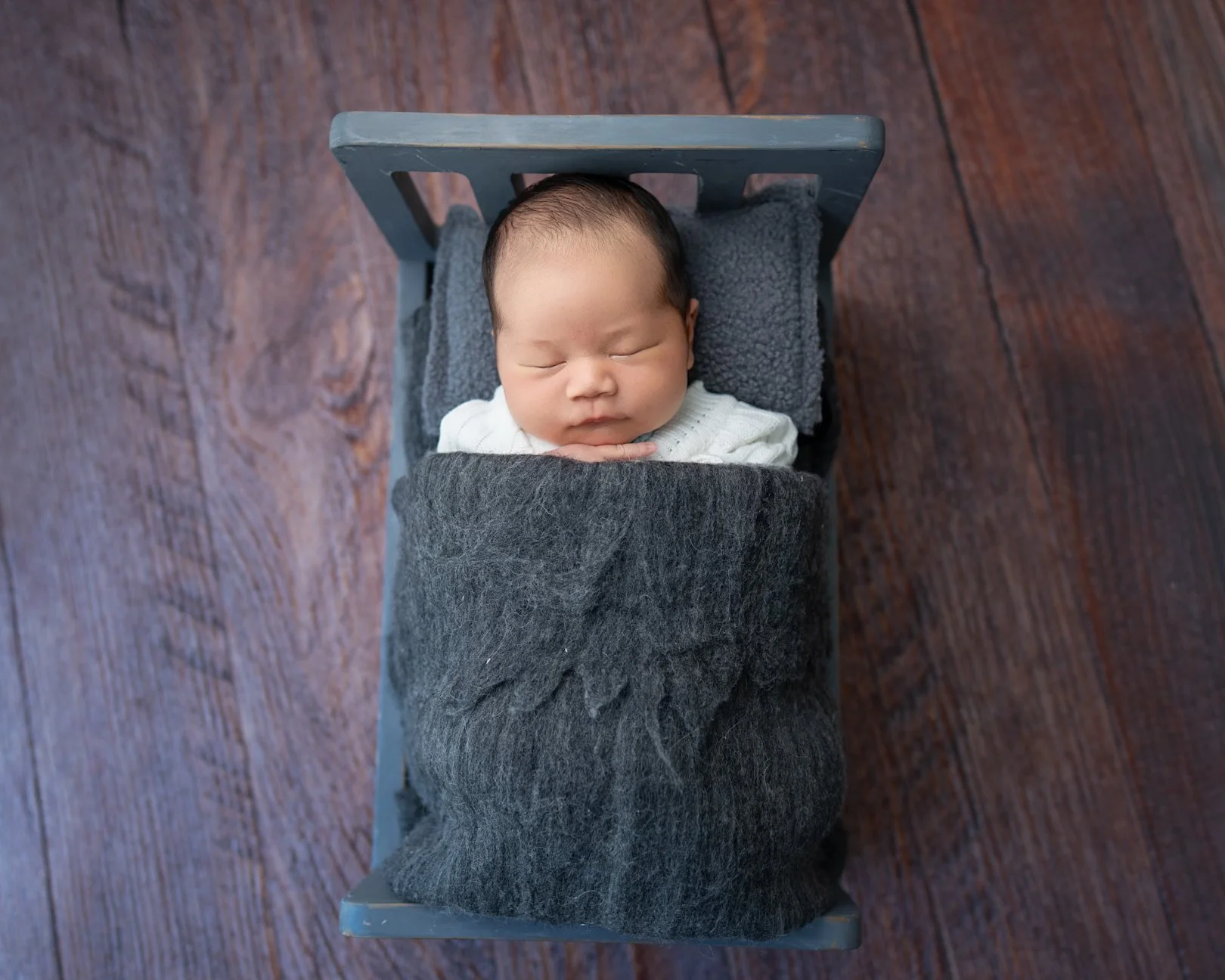 Sleeping newborn baby safely posed in a bed during a West Auckland mobile studio photography session.