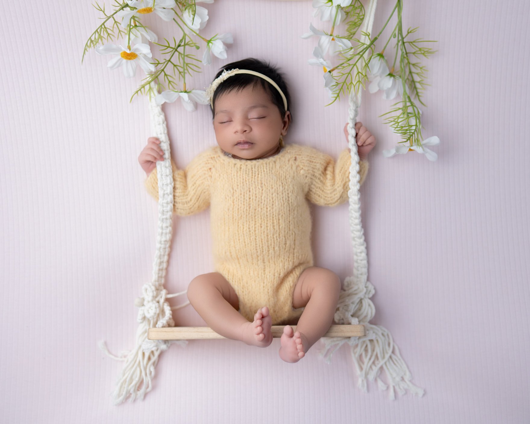Sweet newborn baby girl safely posed on a miniature floral swing prop during a Pakuranga in-home photography session.