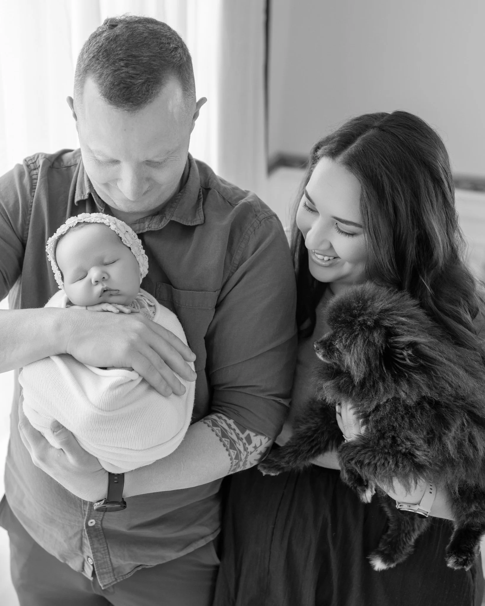 Parents cuddling their newborn baby with their family dog during a relaxed lifestyle newborn photography session in Auckland