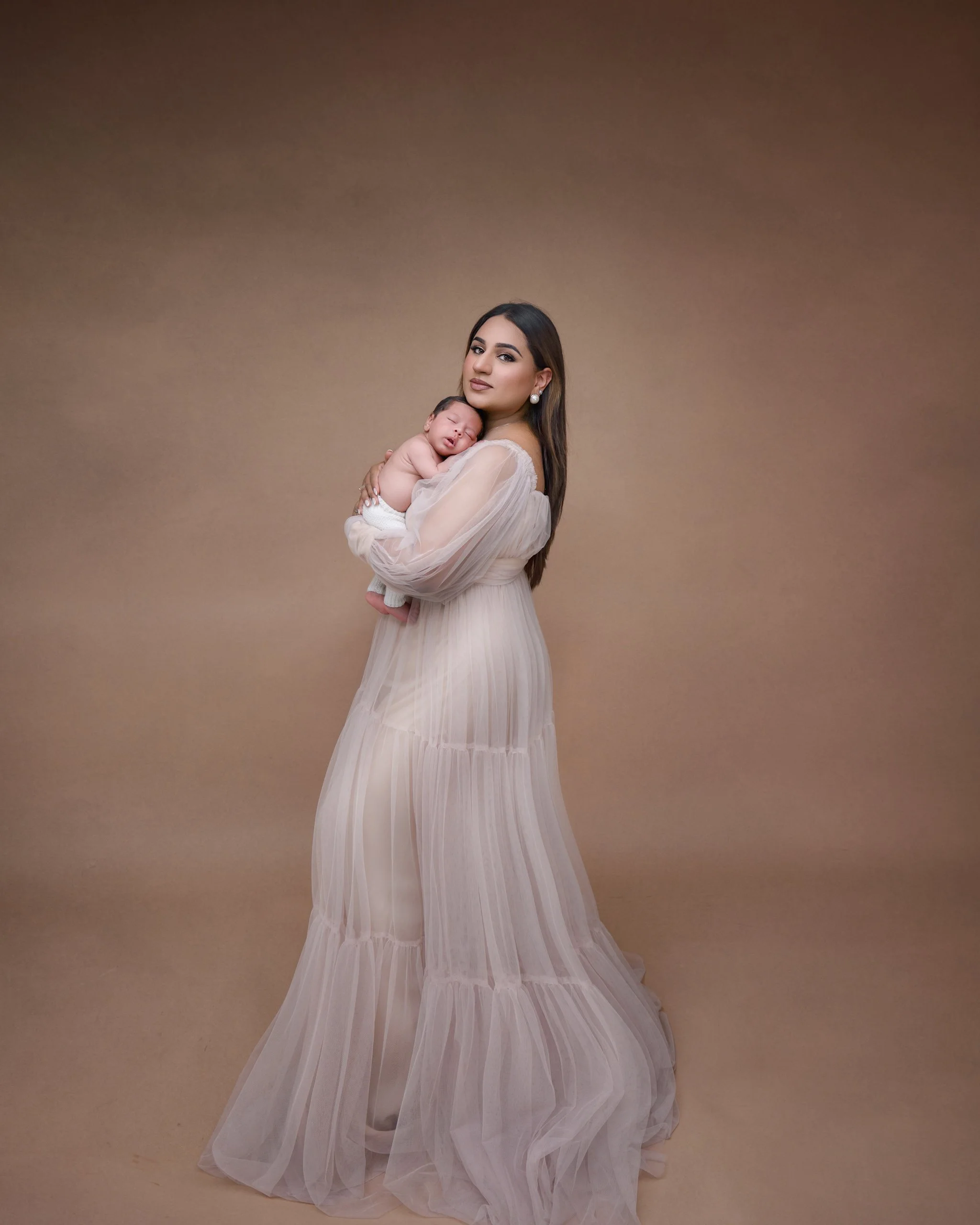 Mother cuddling her newborn in a gown during a studio portrait
