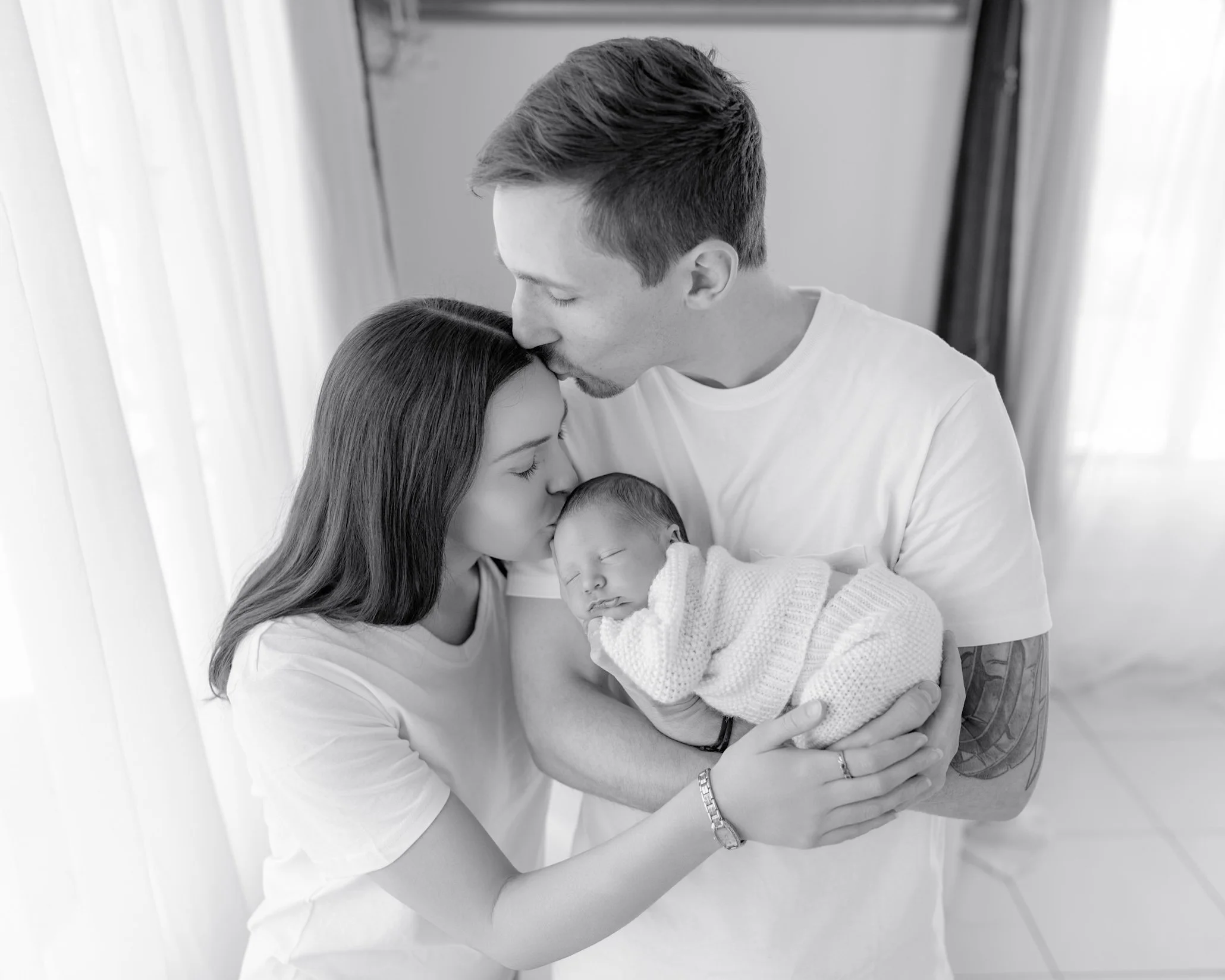 Parents cuddling and kissing their sleeping newborn baby during a guided lifestyle session