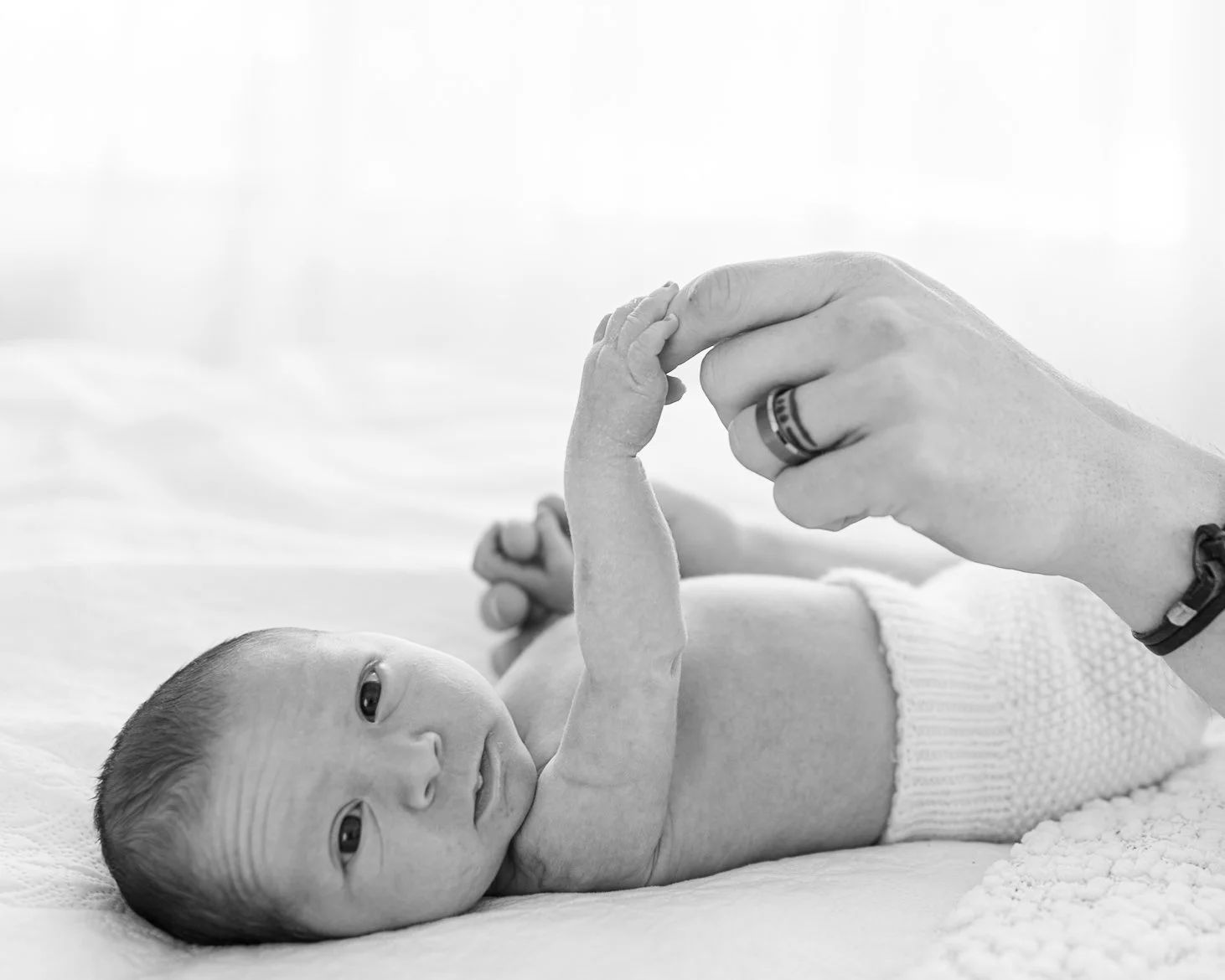 Awake newborn baby reaching for a parent’s hand during a relaxed lifestyle session