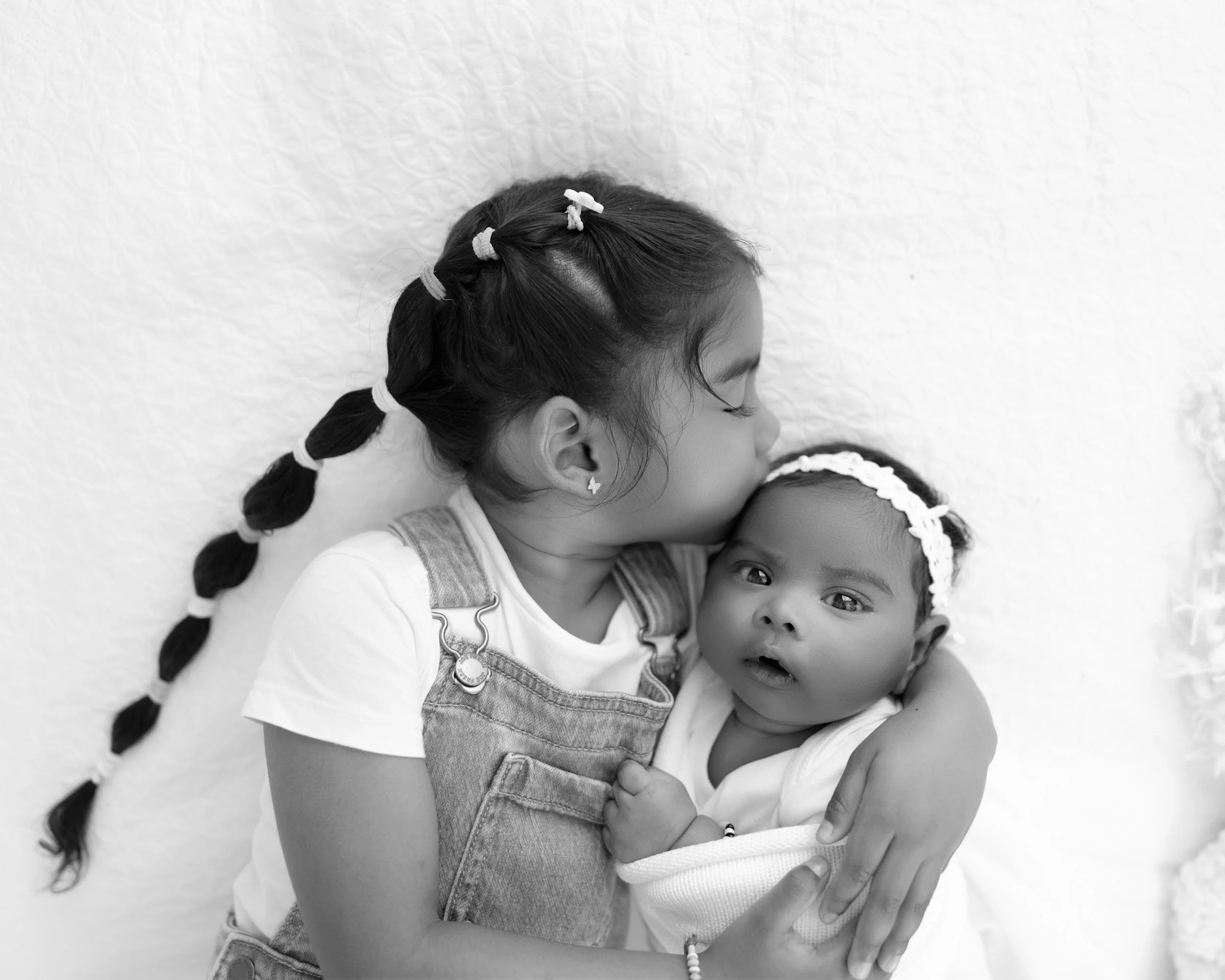 Heartwarming portrait of an older sister kissing her newborn sibling during a lifestyle family photoshoot in Botany.