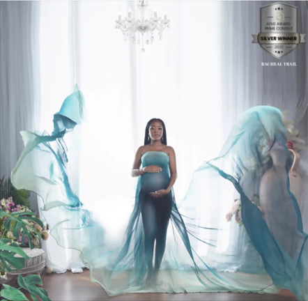 A pregnant woman standing in a bright room with two large, flowing, semi-transparent sculptures on either side, one of a woman with a hat and the other of a woman with wings, with a chandelier hanging from the ceiling and a badge indicating a Silver 
