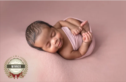 A newborn baby sleeping on a pink surface with a 