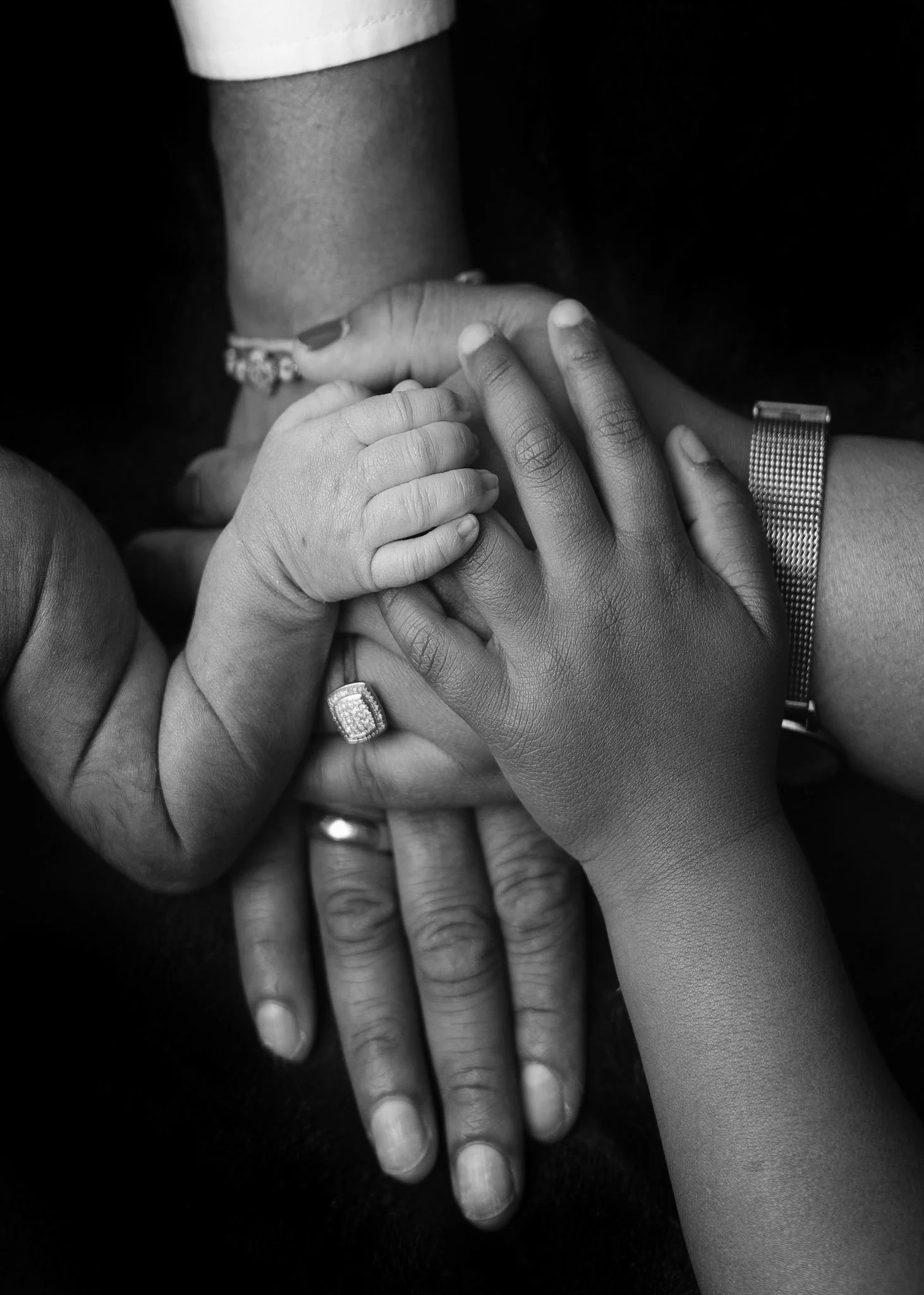 Newborn baby’s tiny hand surrounded by family hands during an Auckland newborn photography session.