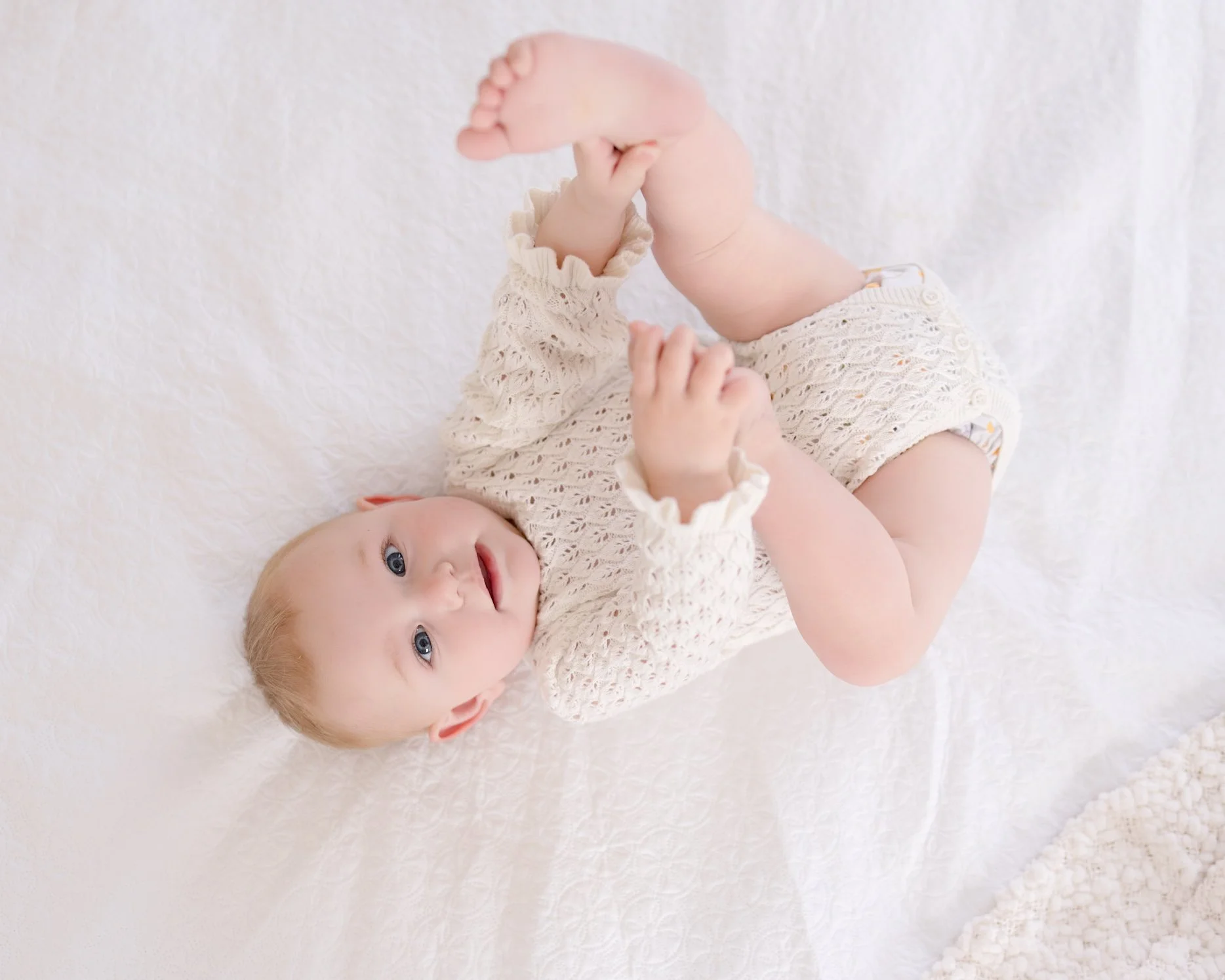 Baby lying on a soft white bed during a relaxed milestone photography session in South Auckland