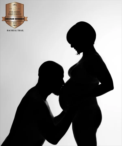 Silhouette of a man kneeling and holding a pregnant woman's belly, with a badge indicating a bronze award for a photo contest.