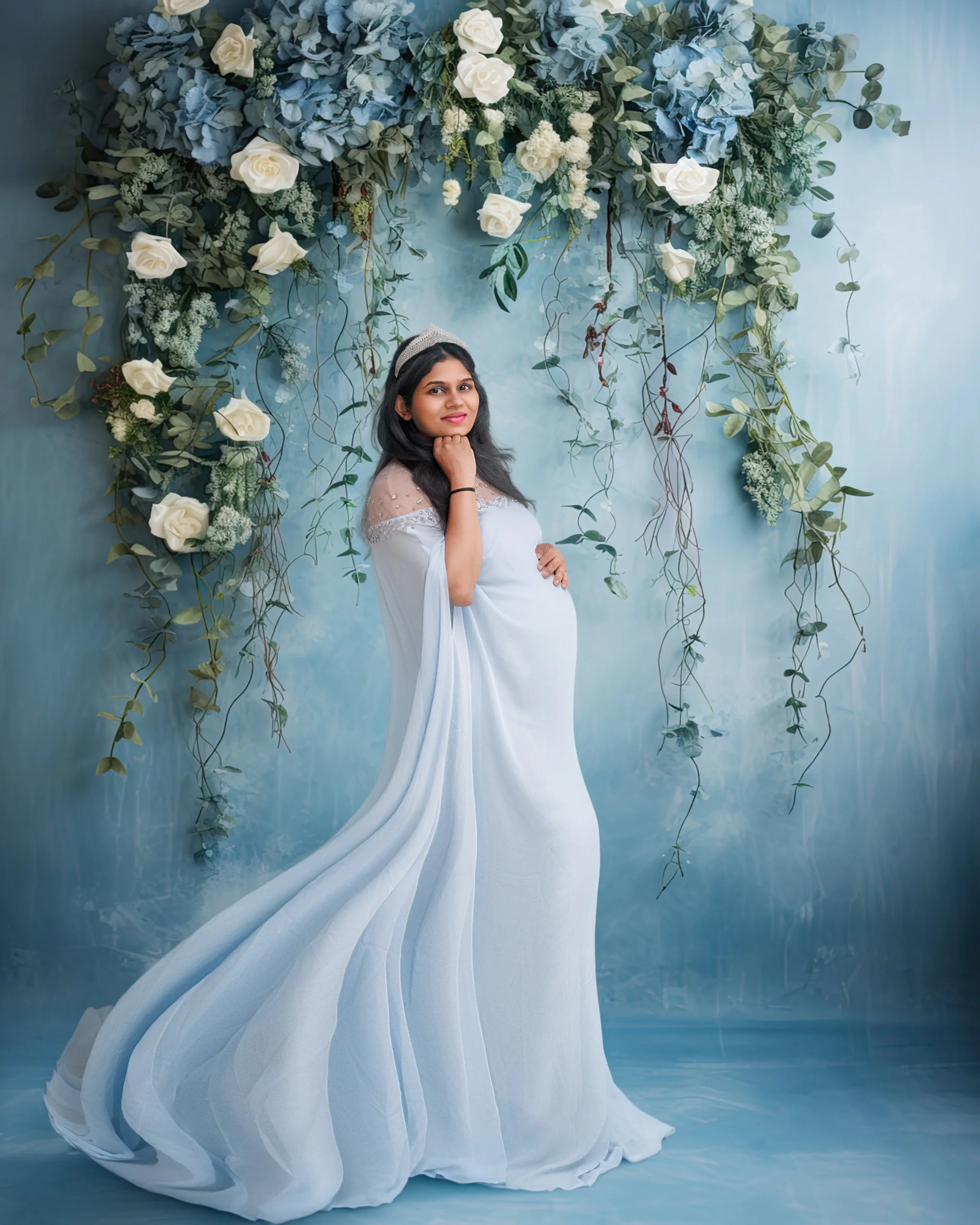 Fine-art maternity portrait in a flowing pale blue gown with floral backdrop during an Auckland studio maternity session