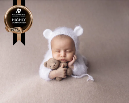 A sleeping baby wearing a white bear hat and holding a small stuffed animal, with a highly recommended badge from Asia Pacific Awards 2021 in the top left corner.