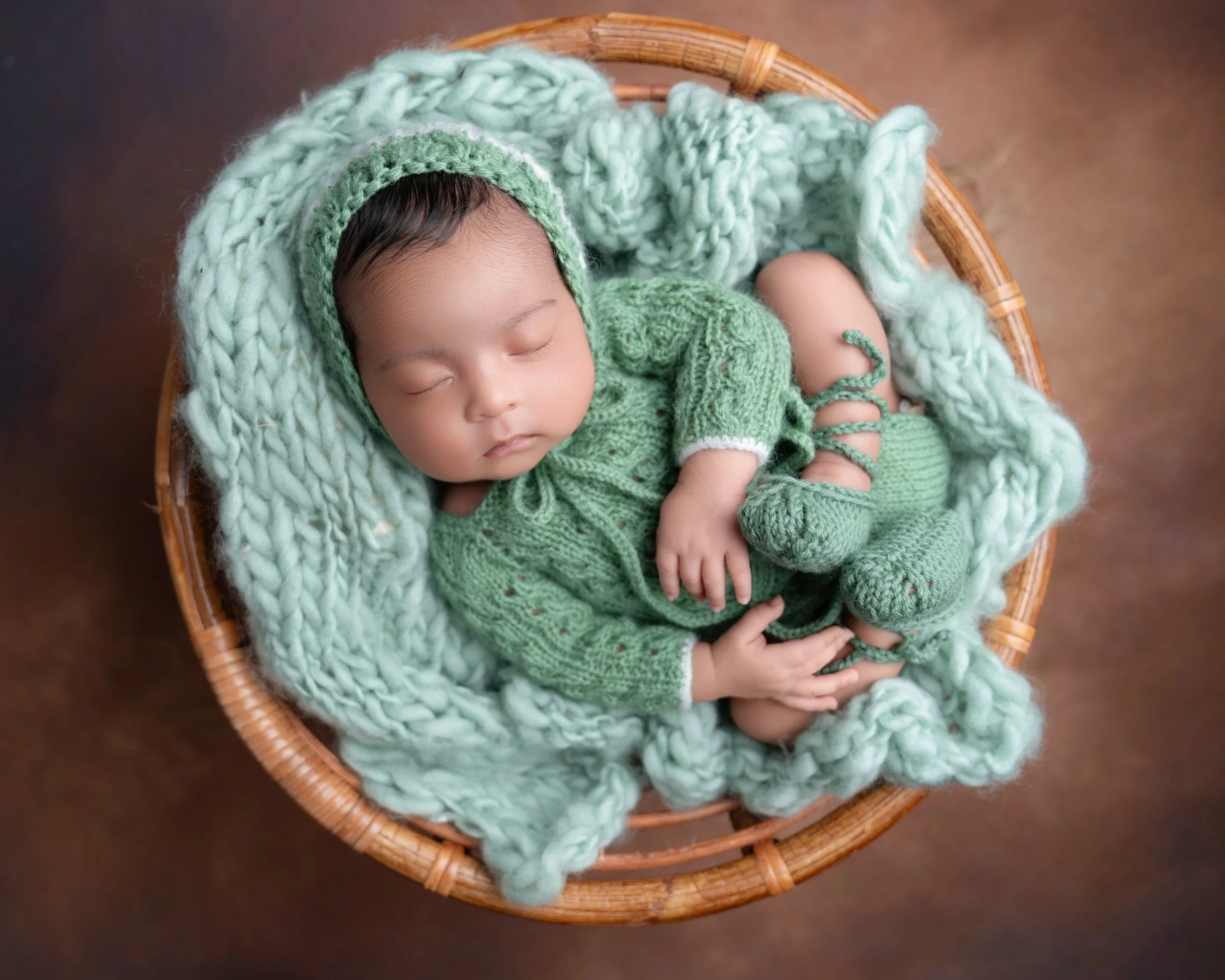  Sleeping newborn baby in a green knitted outfit posed in a wicker basket during an Auckland newborn photoshoot.
Children’s clothing display: