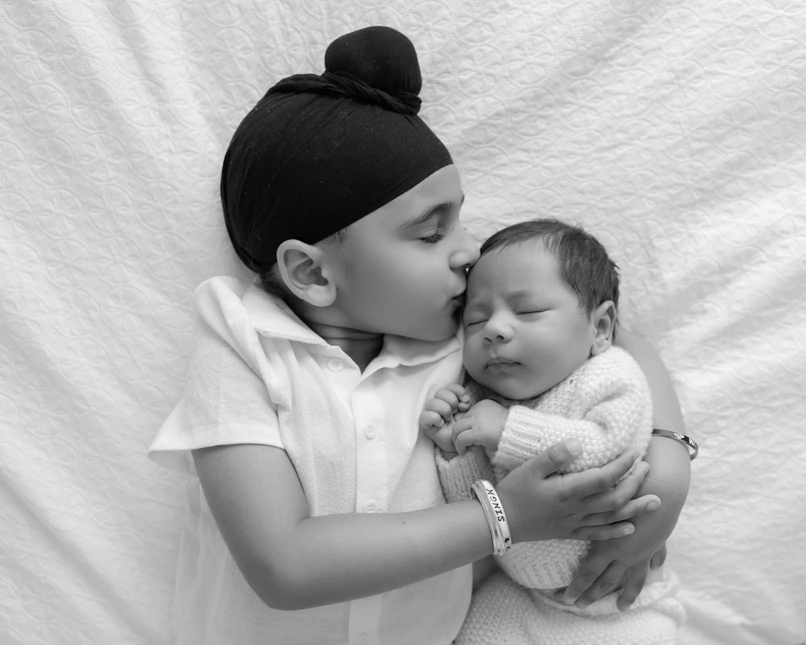 Older sibling cuddling and kissing their newborn baby during a relaxed family newborn session in Auckland.