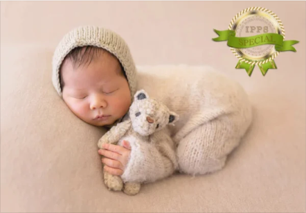 Sleeping baby in a beige knitted hat and sweater, cuddling a small stuffed animal.