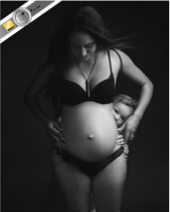 Pregnant woman standing with hands on her belly, looking down.
