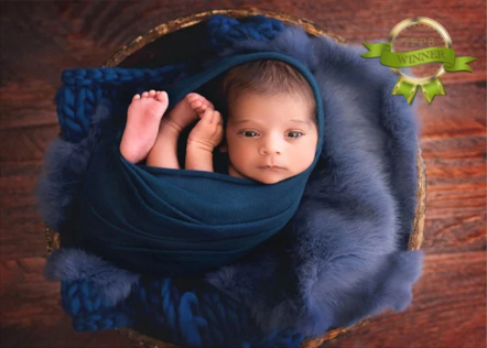 A baby wrapped in a blue blanket, lying in a basket with blue faux fur lining, on a wooden floor.
