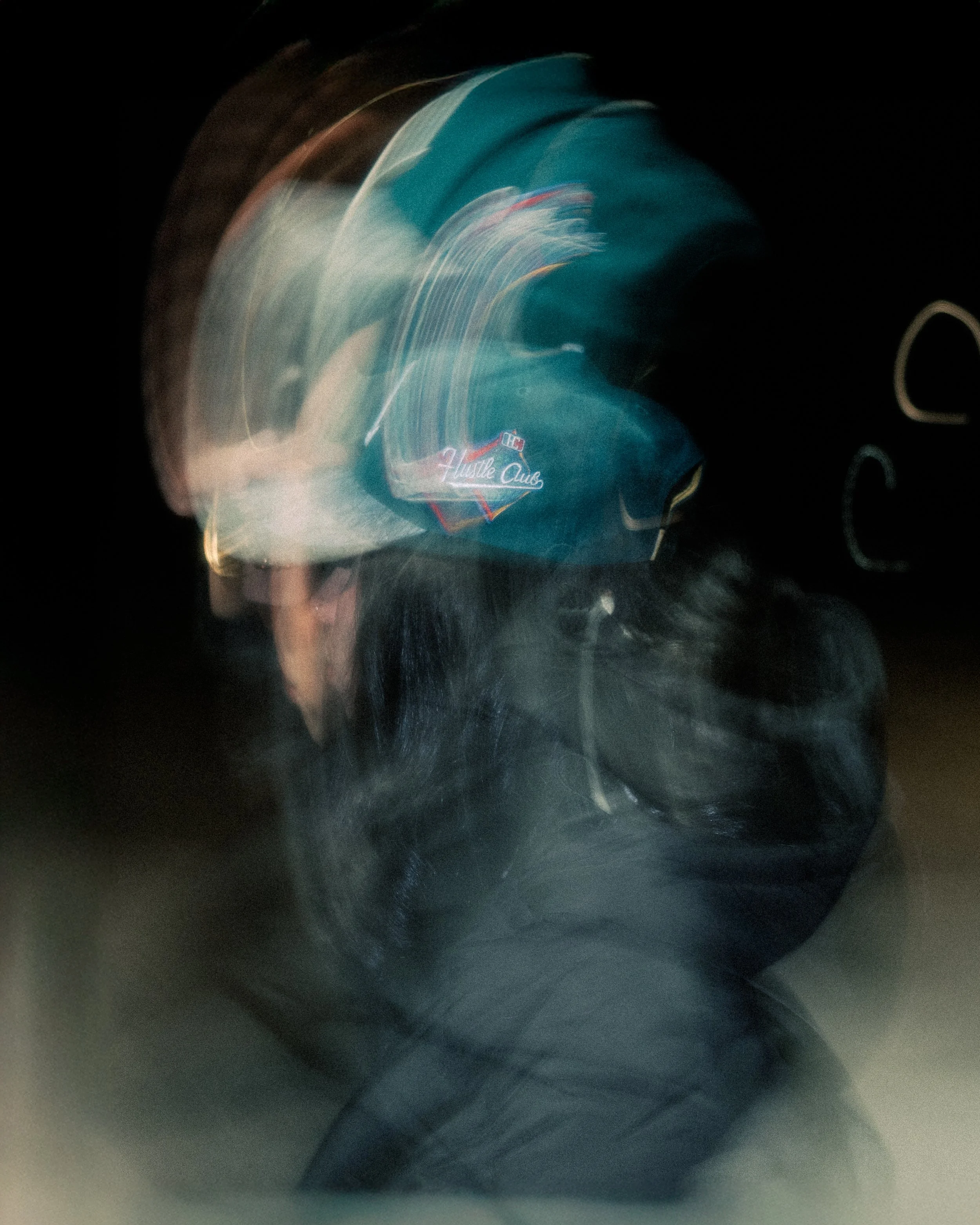 Blurred image of a person wearing a blue hoodie with the logo 'Hustle Club' on it, in a dark environment with motion and light streaks.