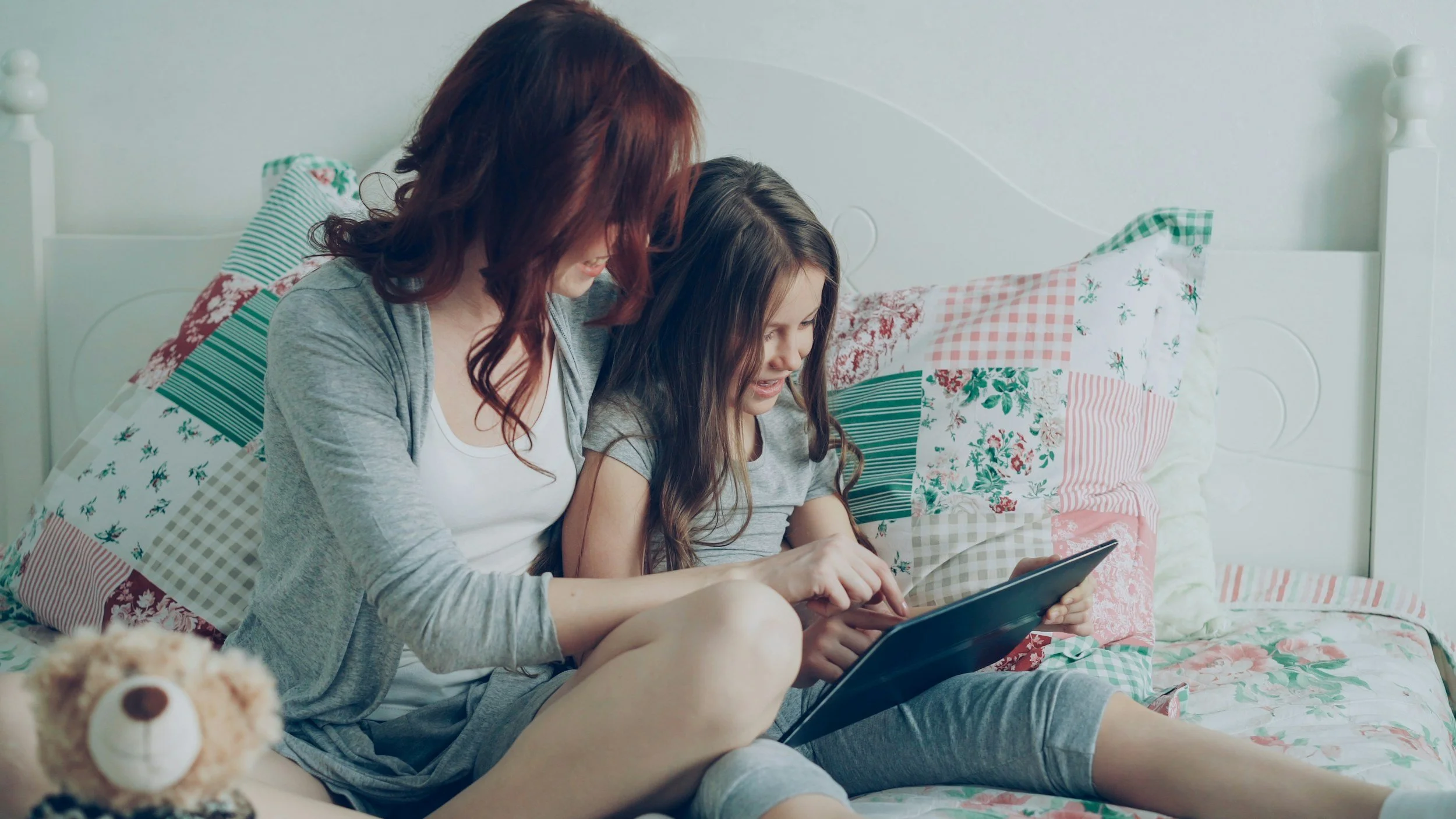 Mother sitting on a bed with quilted bedding holding a tablet, representing reflection and self-awareness for Enneagram moms in motherhood.