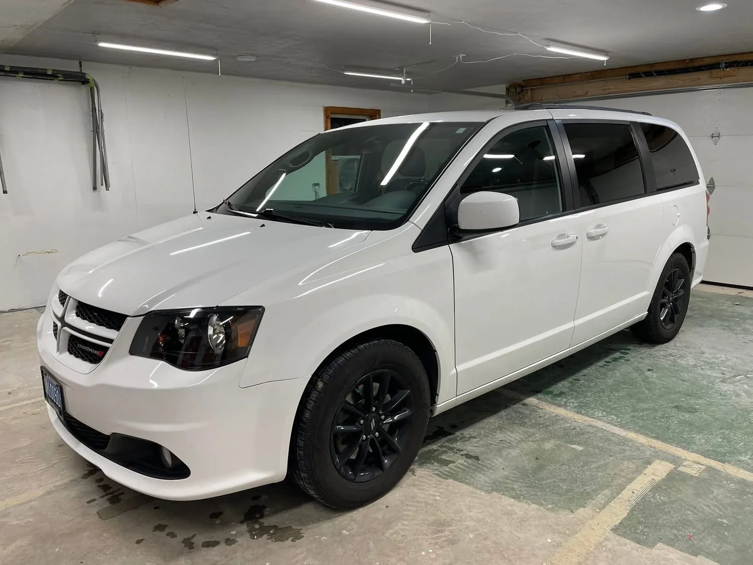 White Dodge Caravan minivan parked in a garage with white walls and a concrete floor.