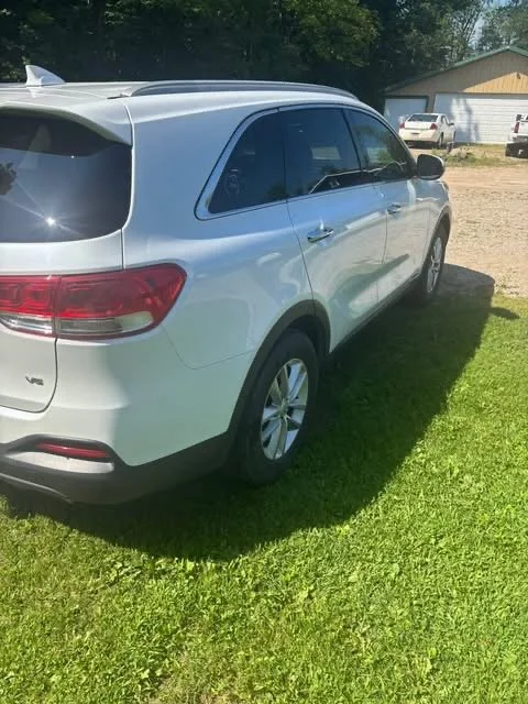 A white KIA Sorento SUV parked on a grassy area near a house with other vehicles in the background.