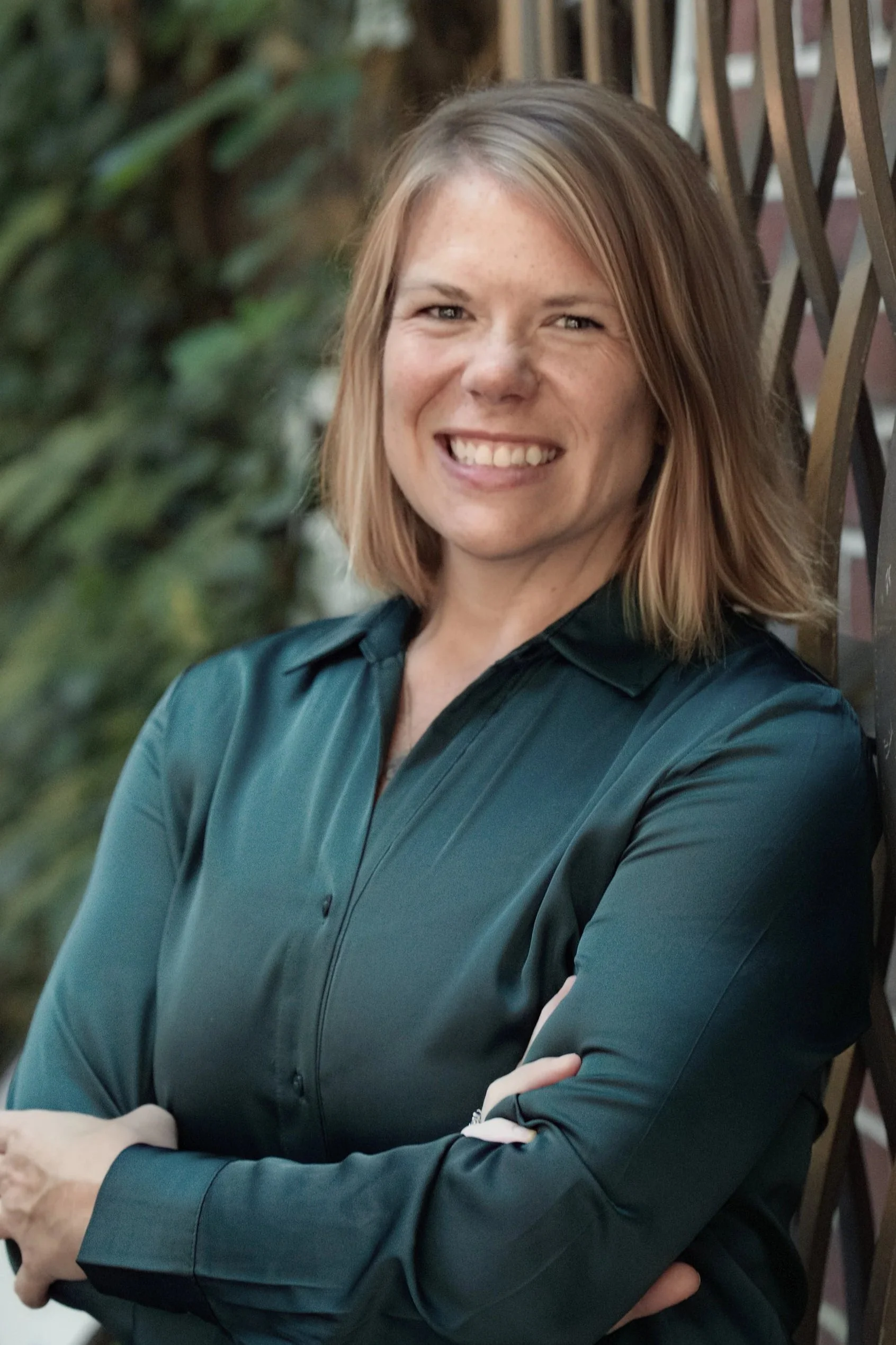 A professional woman with shoulder-length blonde hair, wearing a green blazer and white blouse, smiling at the camera.
