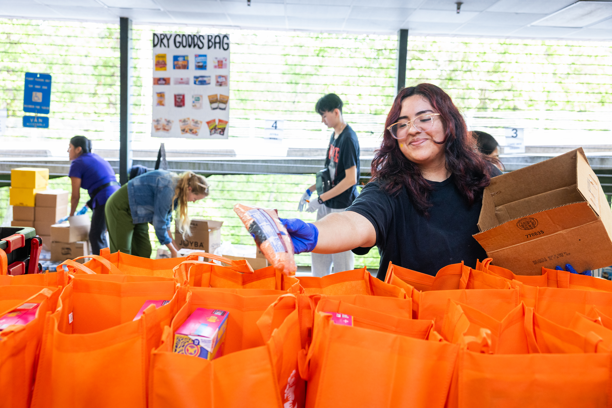People working at a volunteer event packaging food into orange bags at a community center or warehouse.