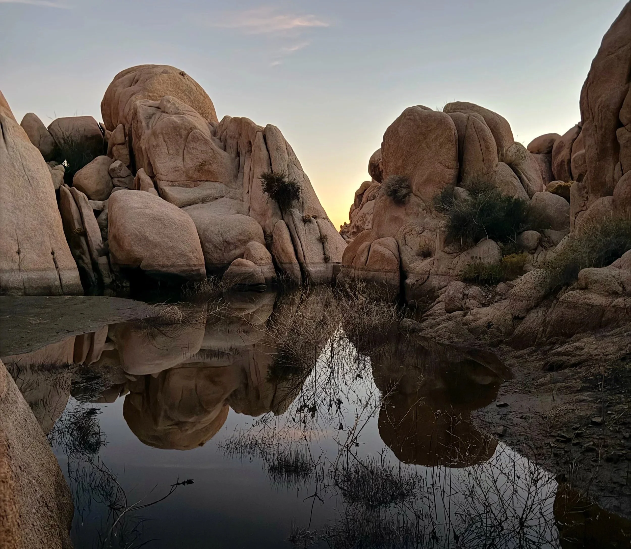 Still desert water reflecting massive boulder formations at Joshua Tree National Park during golden hour