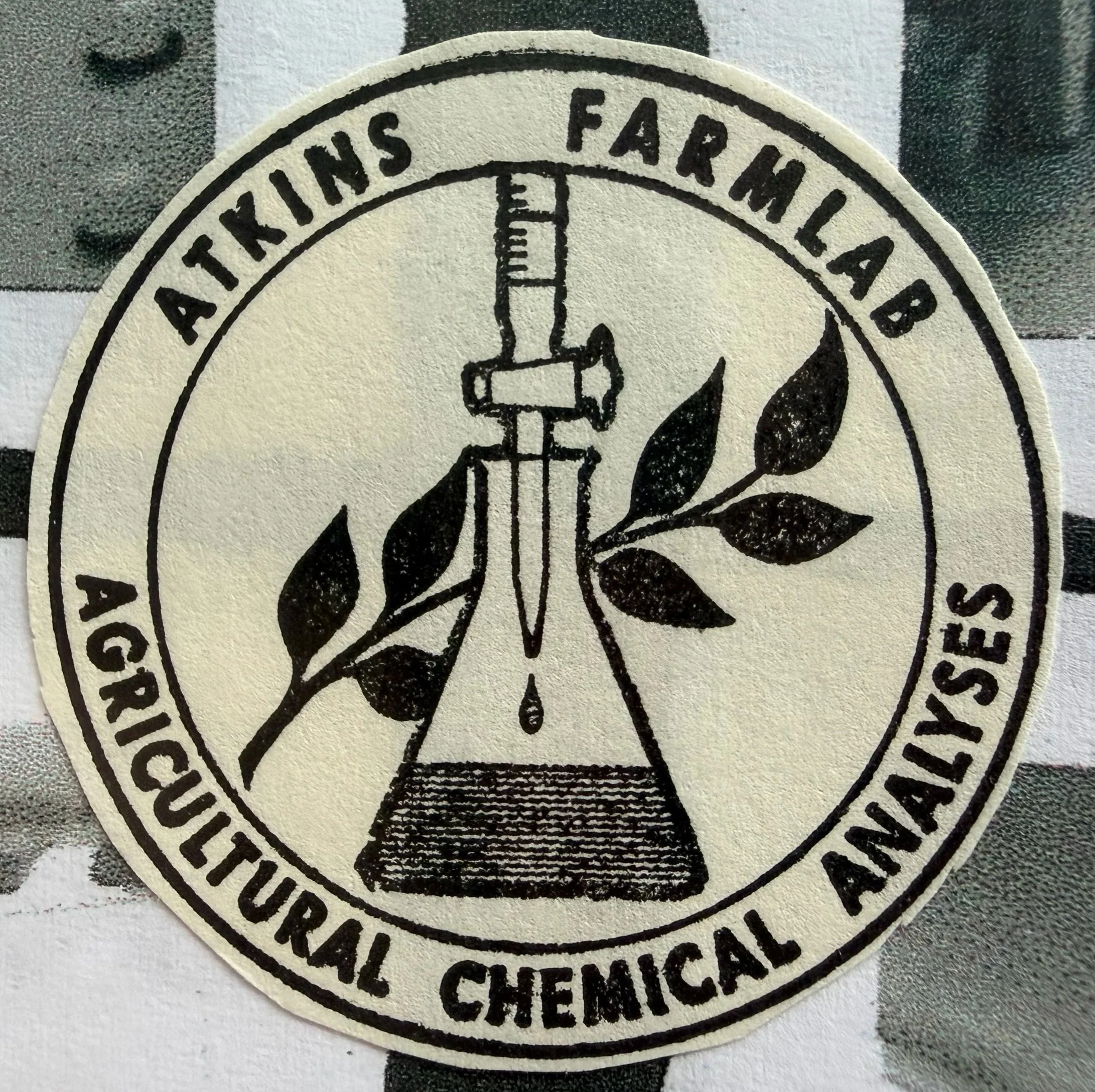A circular emblem for the Agriculture, Animal, and Cultural Chemicals Association featuring a pipette dripping with liquid, a leafy branch, and a chemical flask.