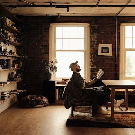 A young man reading a Bible in front of a brick wall, backlit by a vintage window.