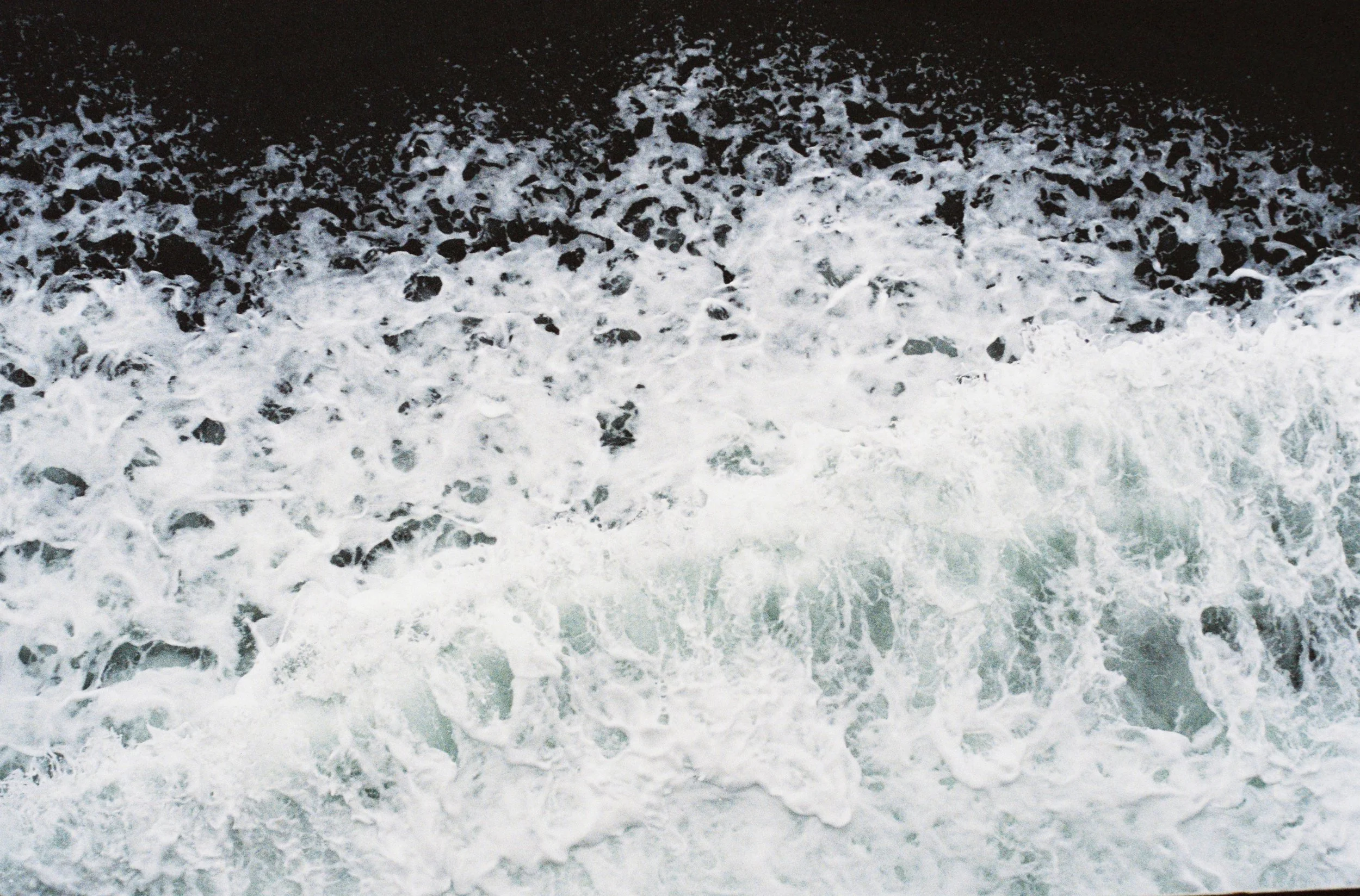 Aerial view of white foamy ocean waves crashing against dark water.