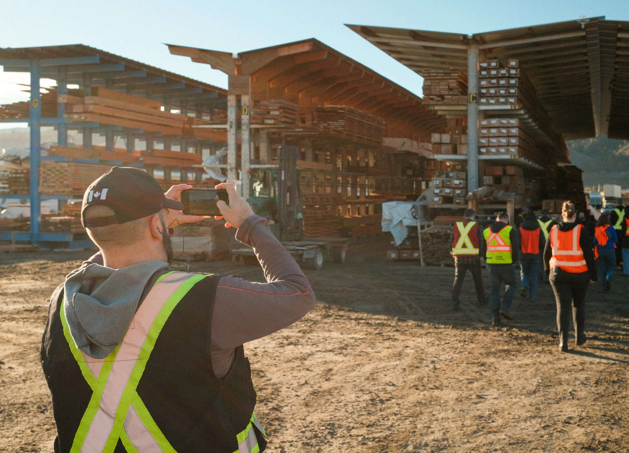 A group of construction workers and engineers at a construction site, with various building materials and partially built structures around them, as one person takes a photo.