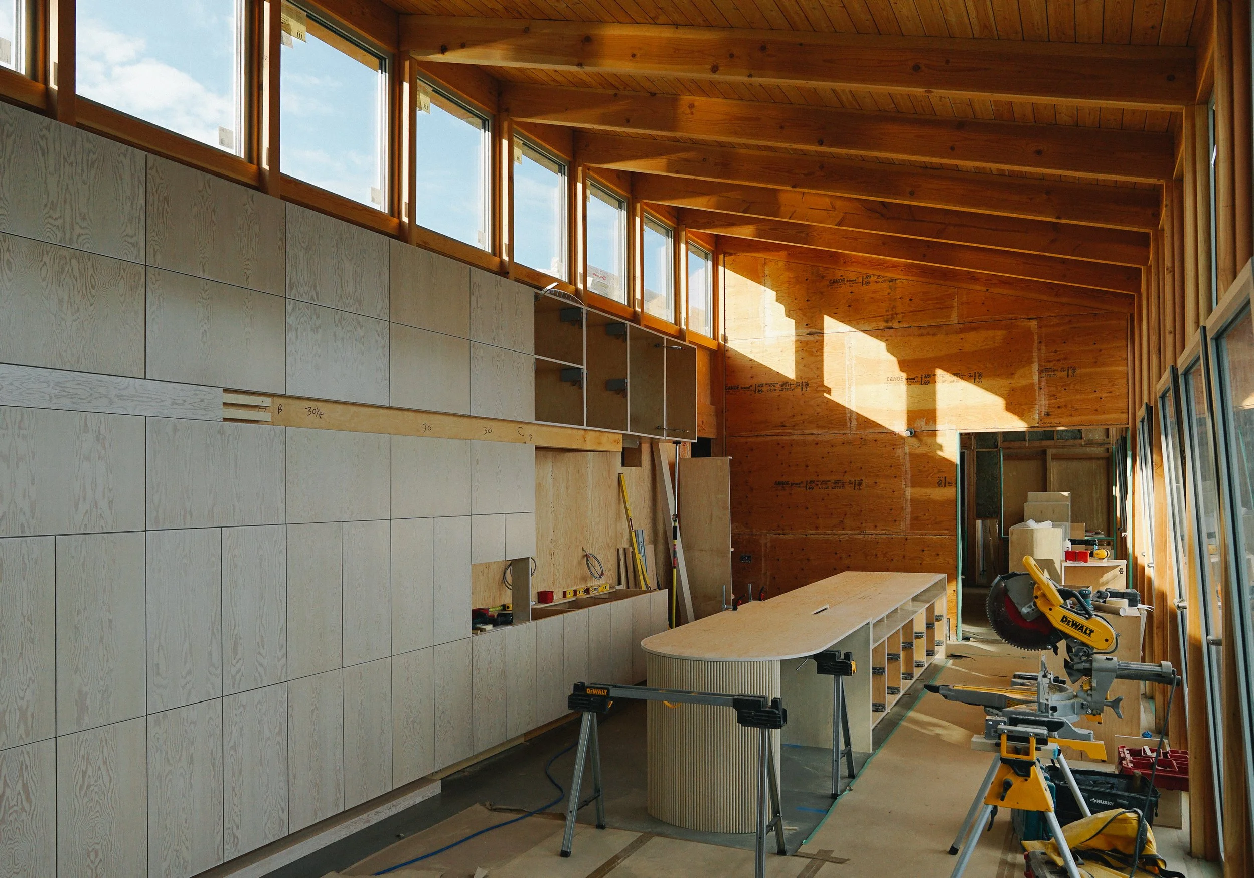 Interior of a construction site with wooden walls and ceiling, large windows at the top, a workbench, and a miter saw.