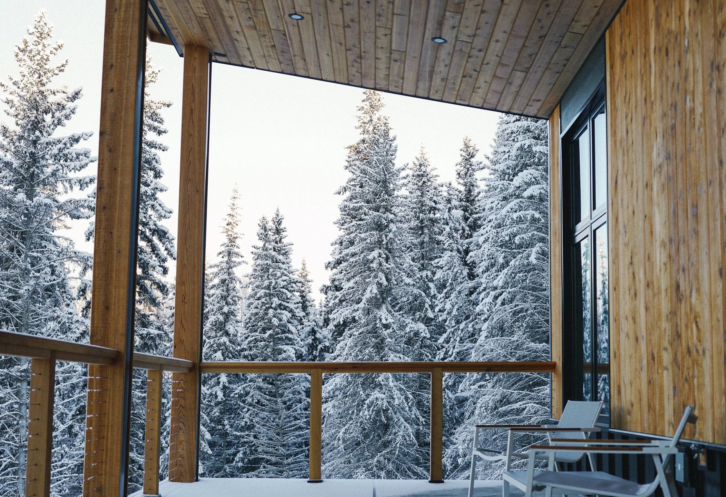 Wooden balcony overlooking snow-covered pine trees during winter.