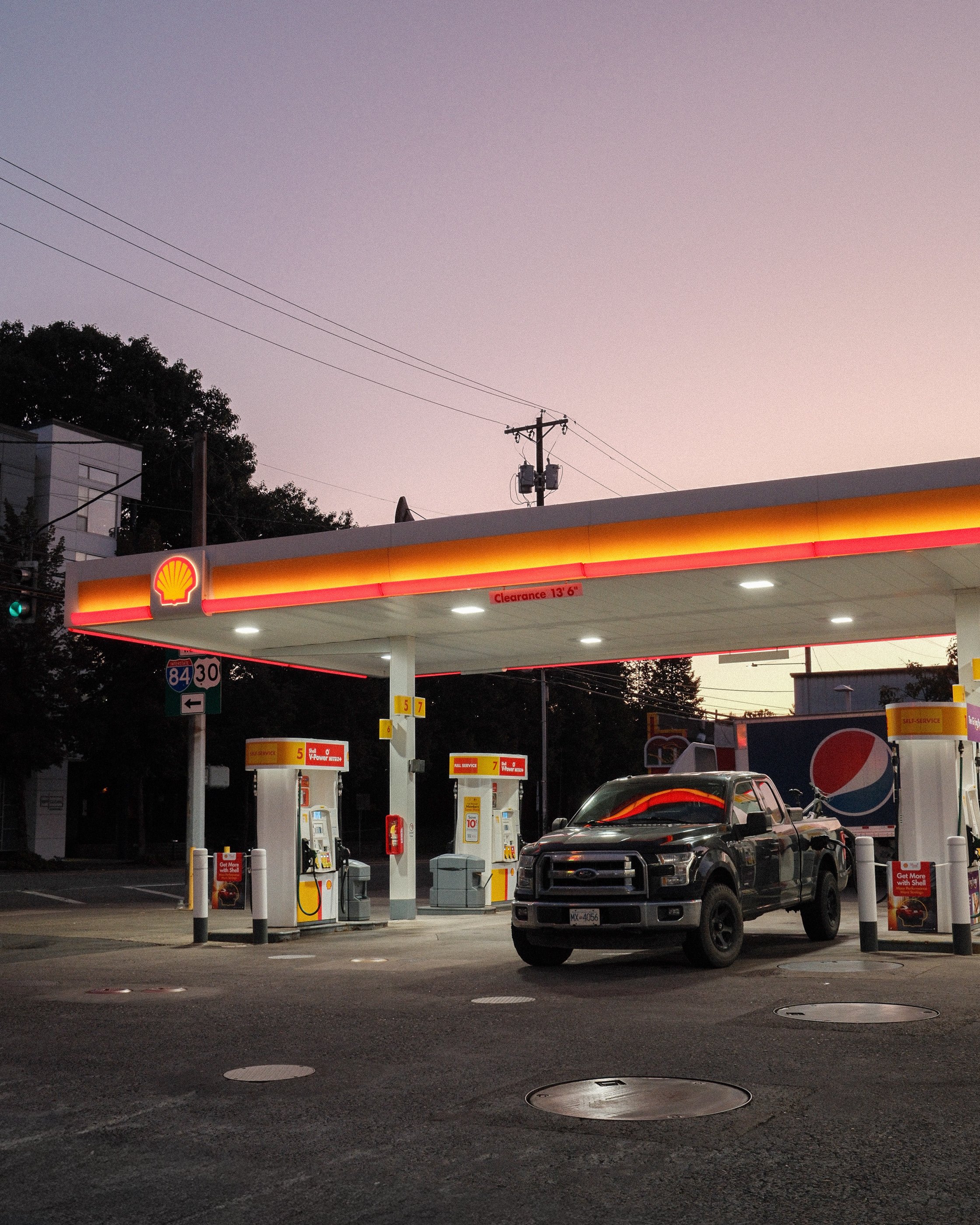Shell gas station at dusk with a black pickup truck parked near fuel pumps.
