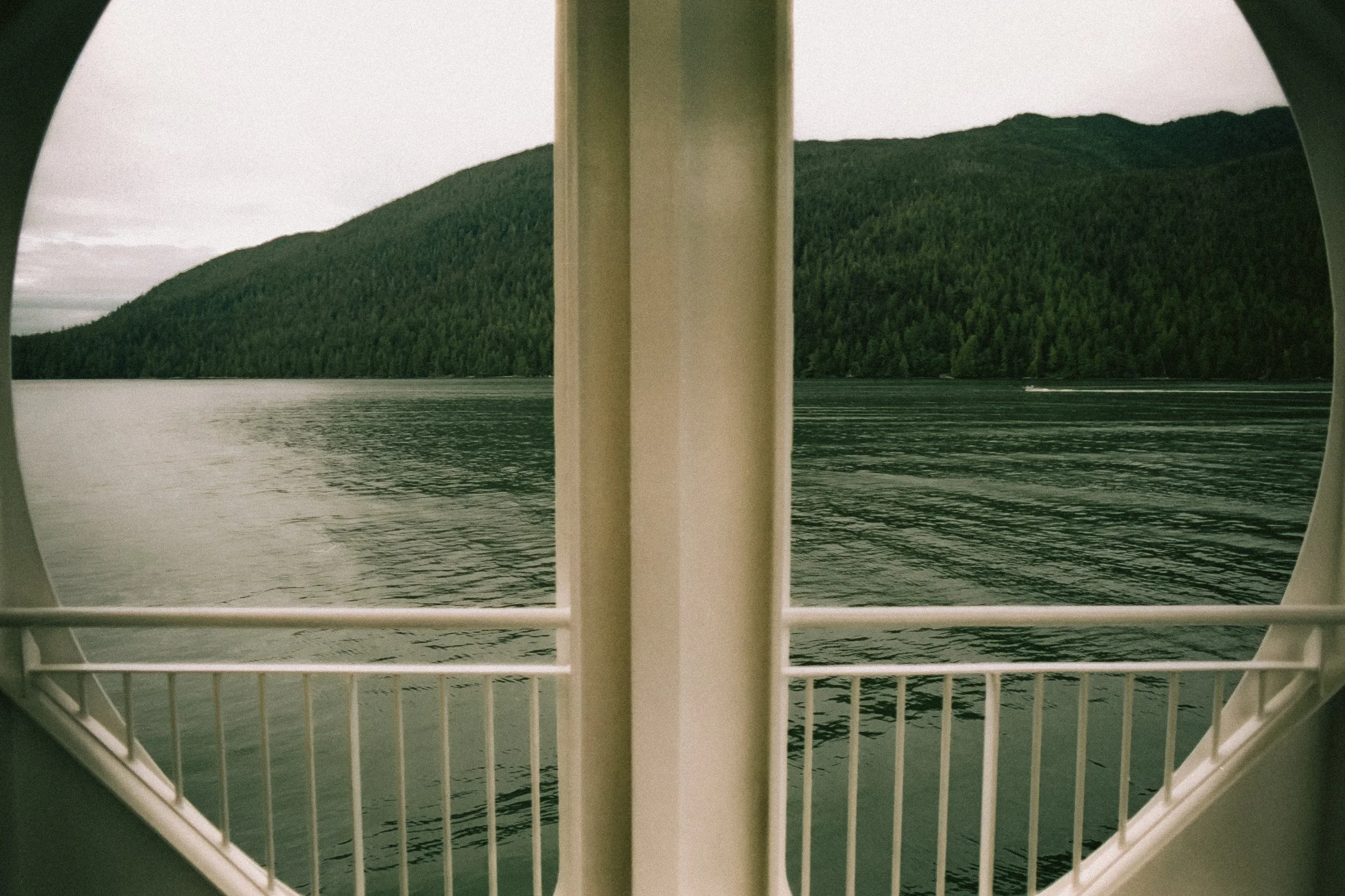 View of a lake and green forested hills through a boat's porthole.