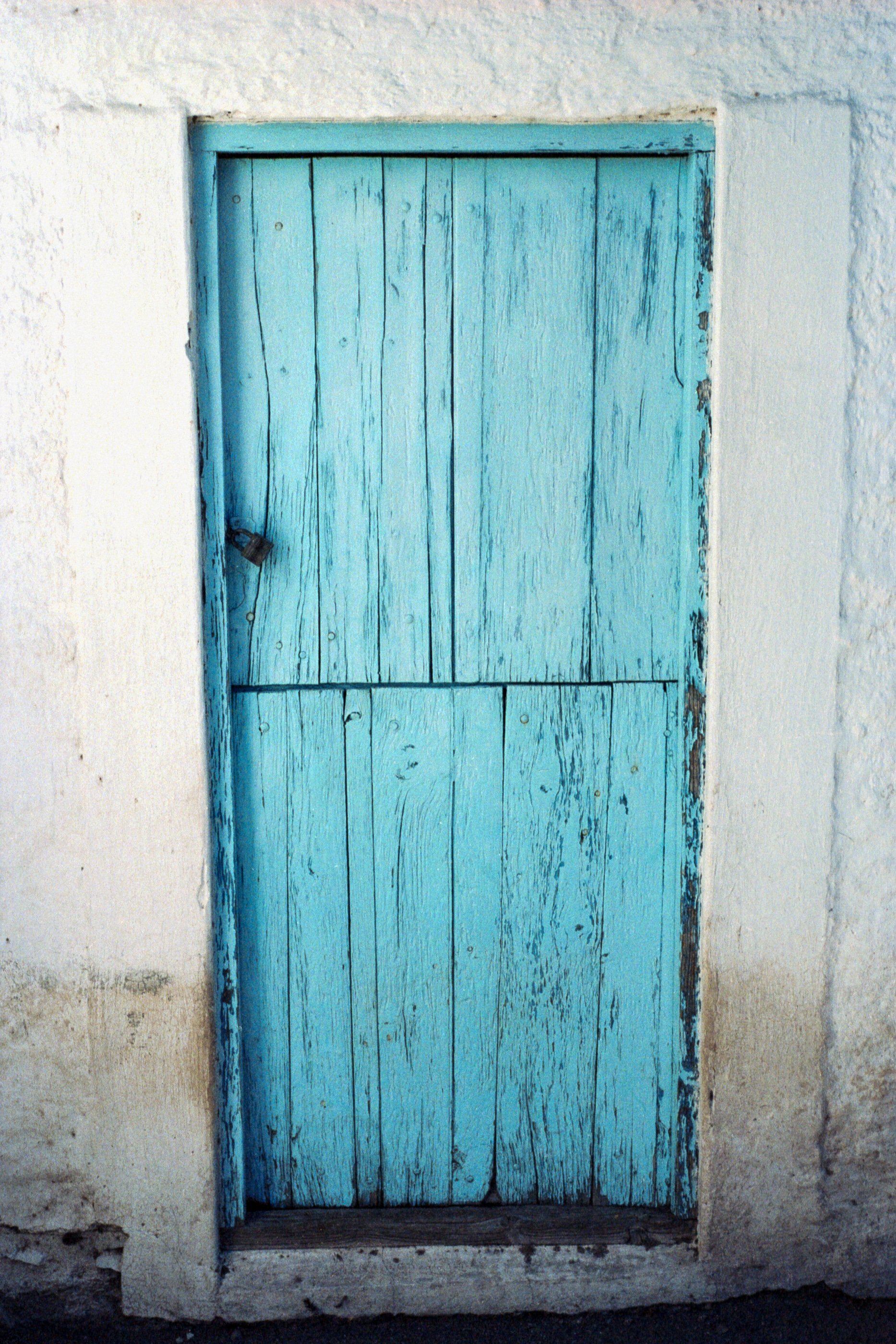 A weathered blue wooden door set in a white stone or stucco wall.