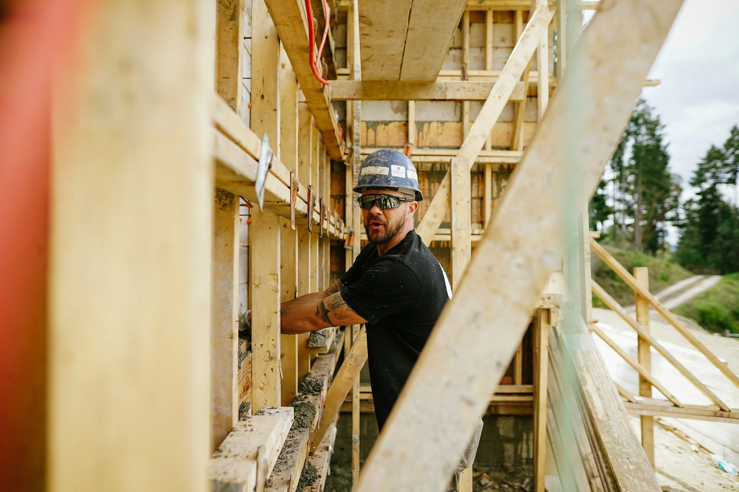 A construction worker wearing a helmet and sunglasses working on framing a building.