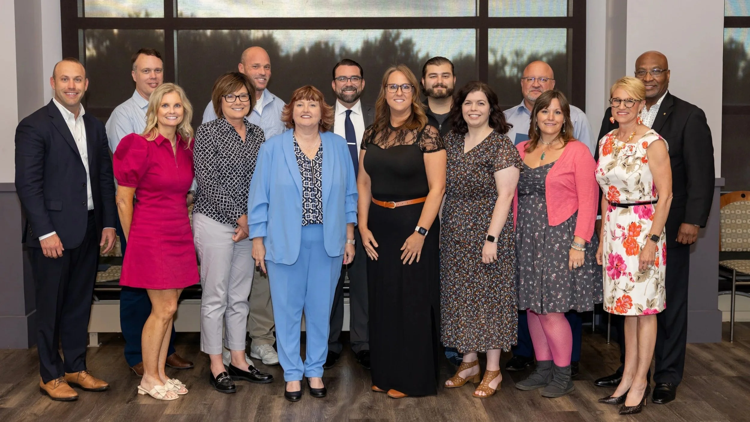 Group of diverse professionals posing indoors in front of large window.
