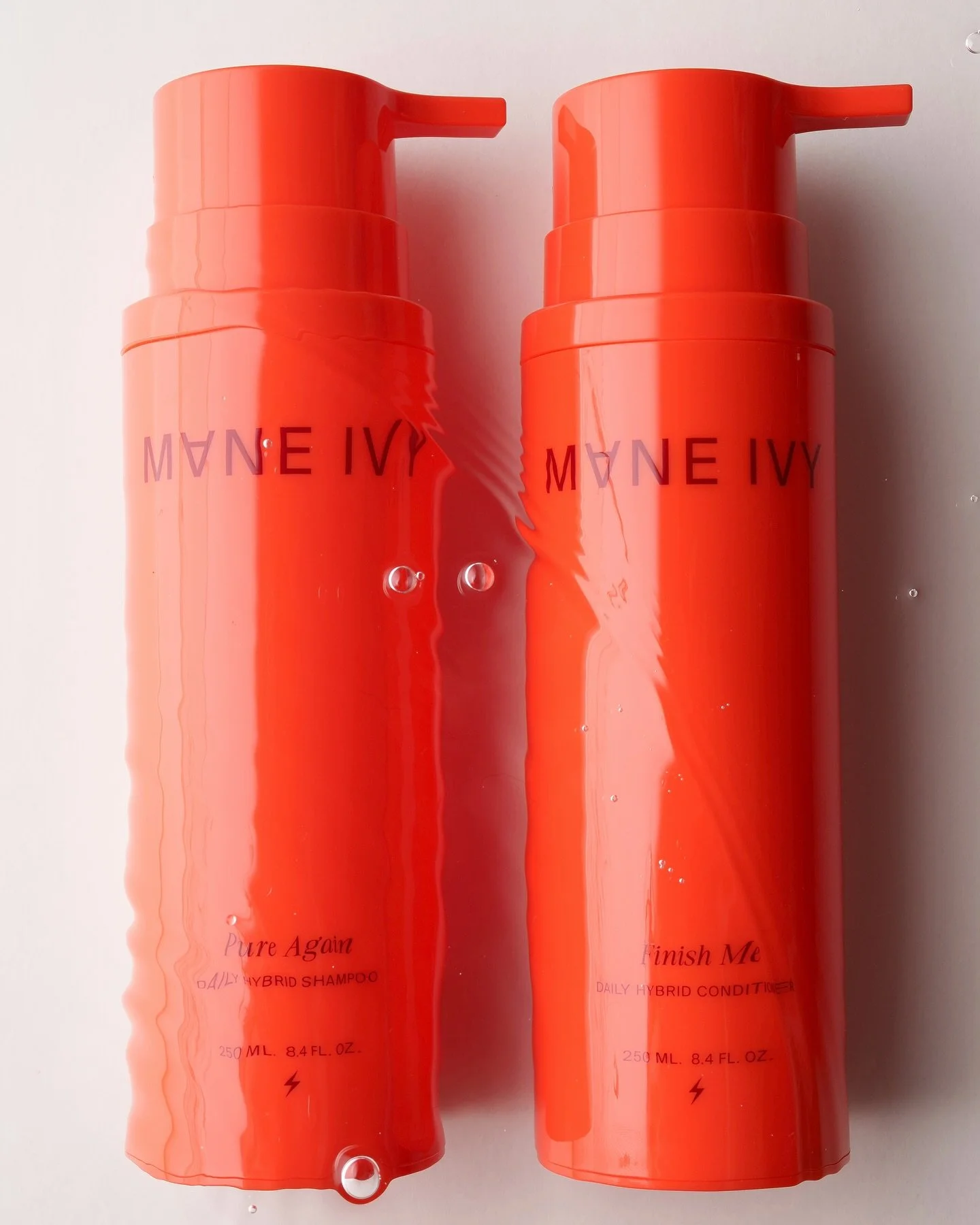 Two orange bottles of HAANE IVY hair care products, one labeled 'Pure Again' Shampoo and the other 'Finish Me' Conditioner, with water droplets on them.