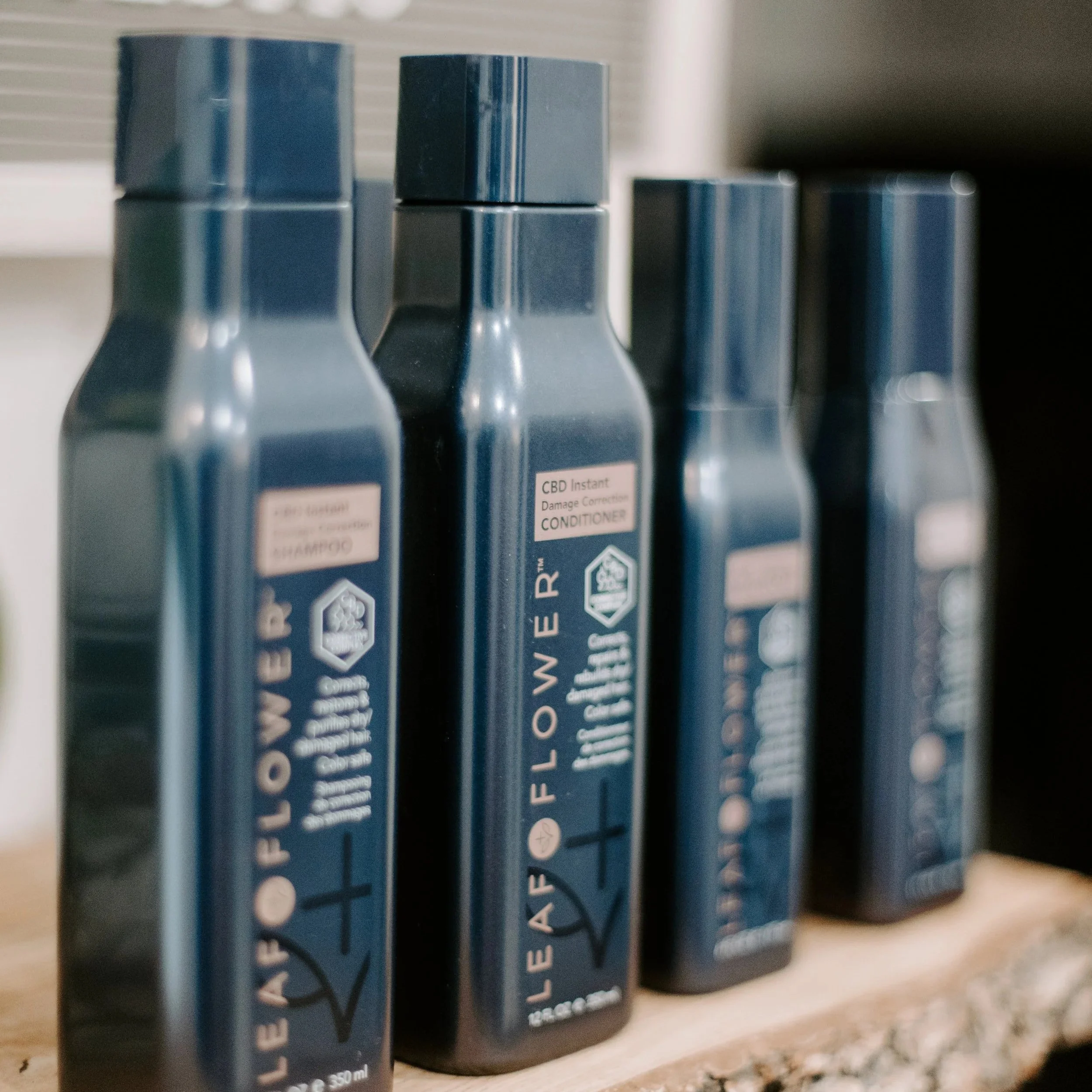 Four blue bottles of Leaf & Flower CBD hair care products on a wooden surface.