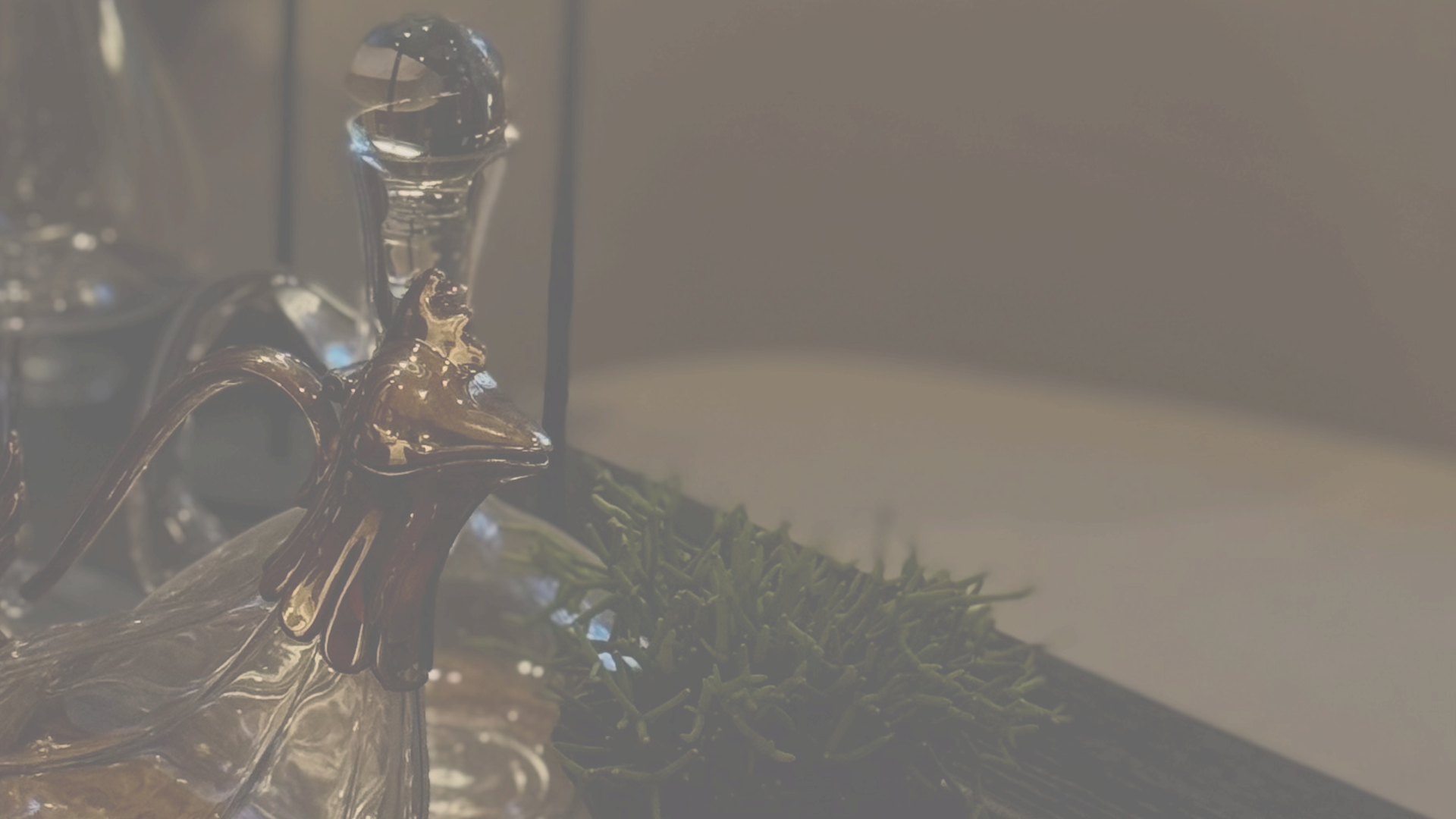 Figura decorativa de um pássaro de vidro com acabamento dourado, ao lado de uma suculenta em um ambiente com iluminação baixa.