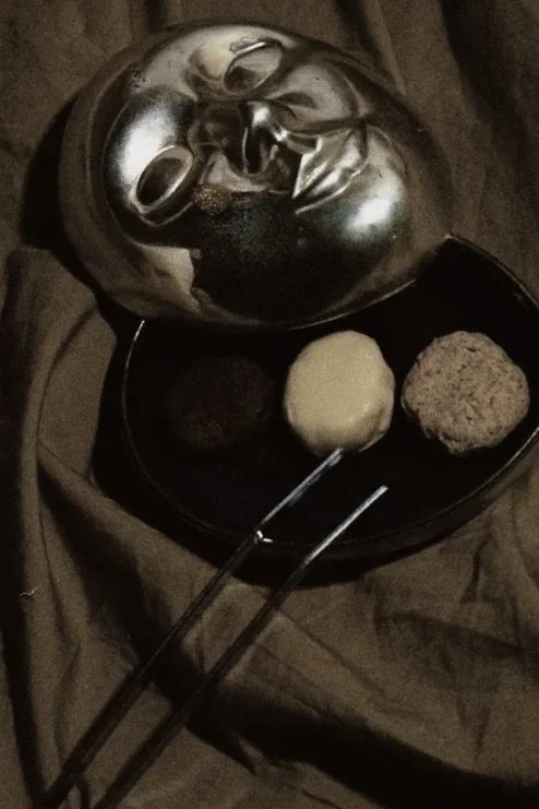 Máscara de rosto de metal de The Phantom of the Opera ao lado de uma bandeja com três alimentos e dois palitos de comida.