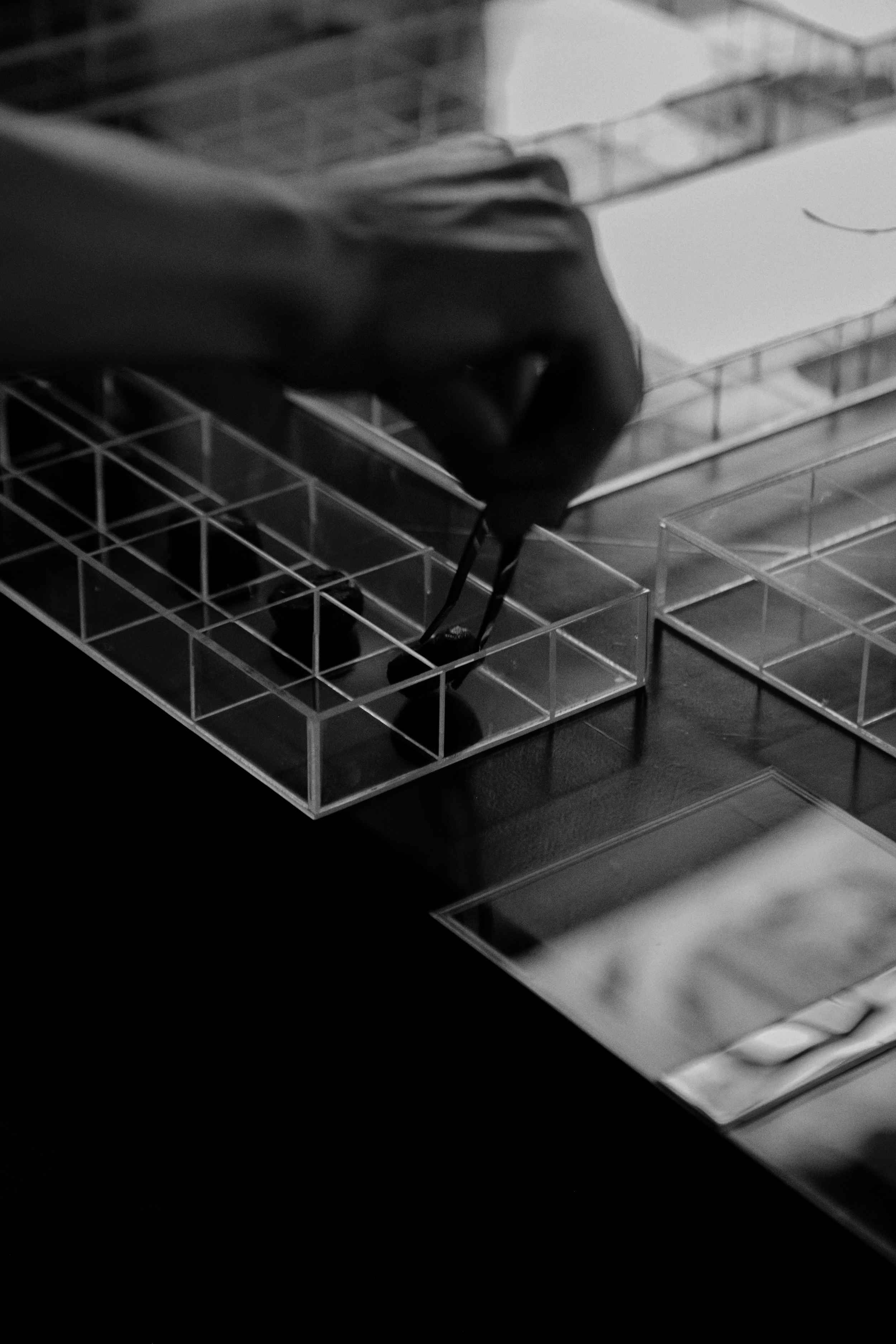 Mão segurando pinça, manipulando objetos em uma bancada com divisórias de acrílico.